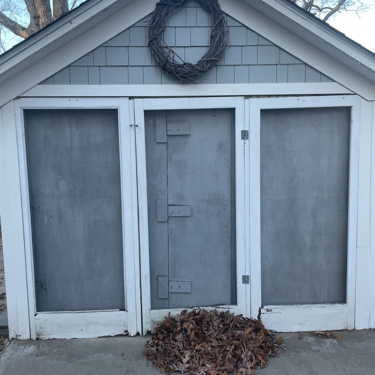 Weathered shed facade with peeling gray panel doors before renovation