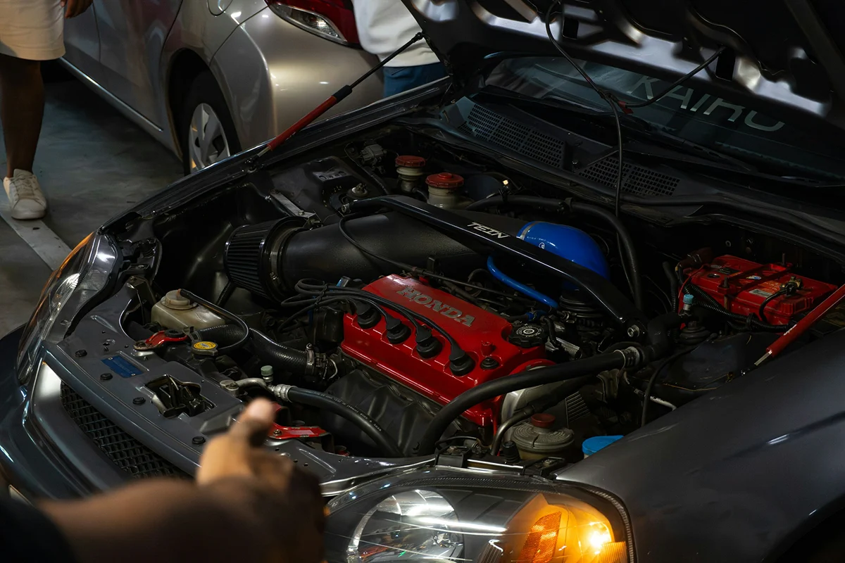 Engine bay cleaning service with technician inspecting and detailing vehicle components.