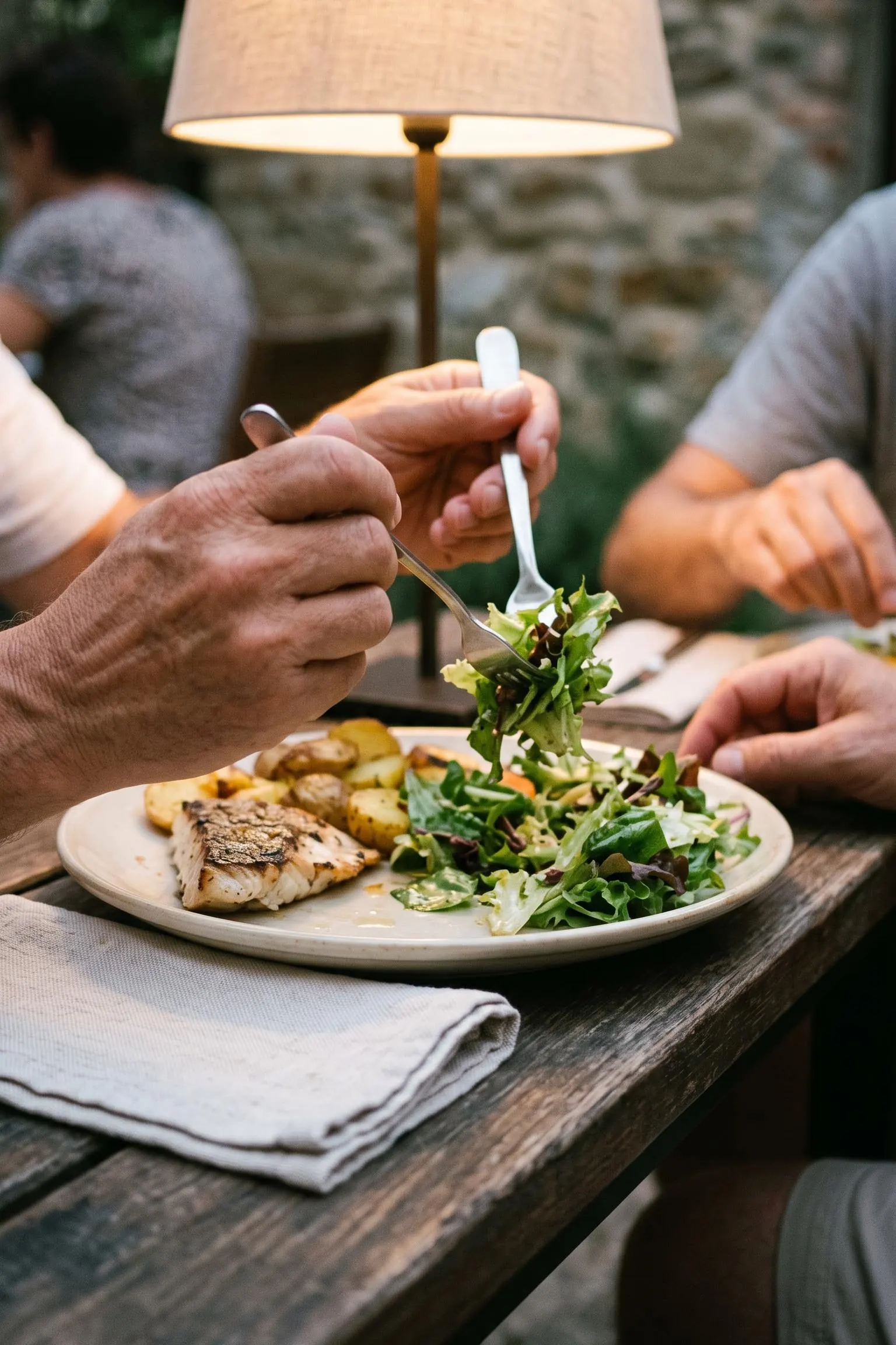 Close view from above of hands lifting a forkful of salad at the start of an evening meal outdoors