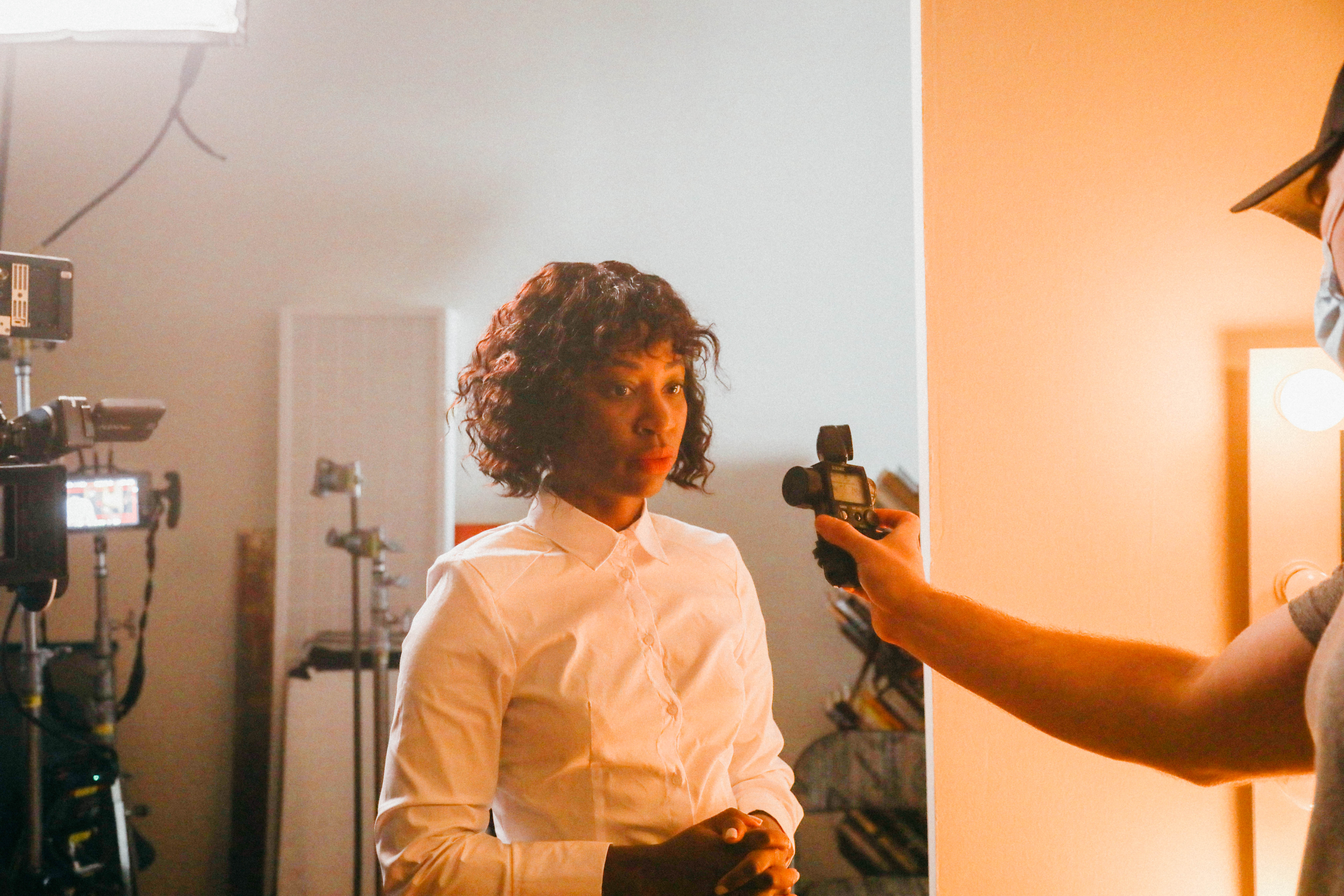 Natasha Ofili, in a white shirt, stands under lighting equipment, with Cooper Ulrich, Director of Photography, holding a light meter.