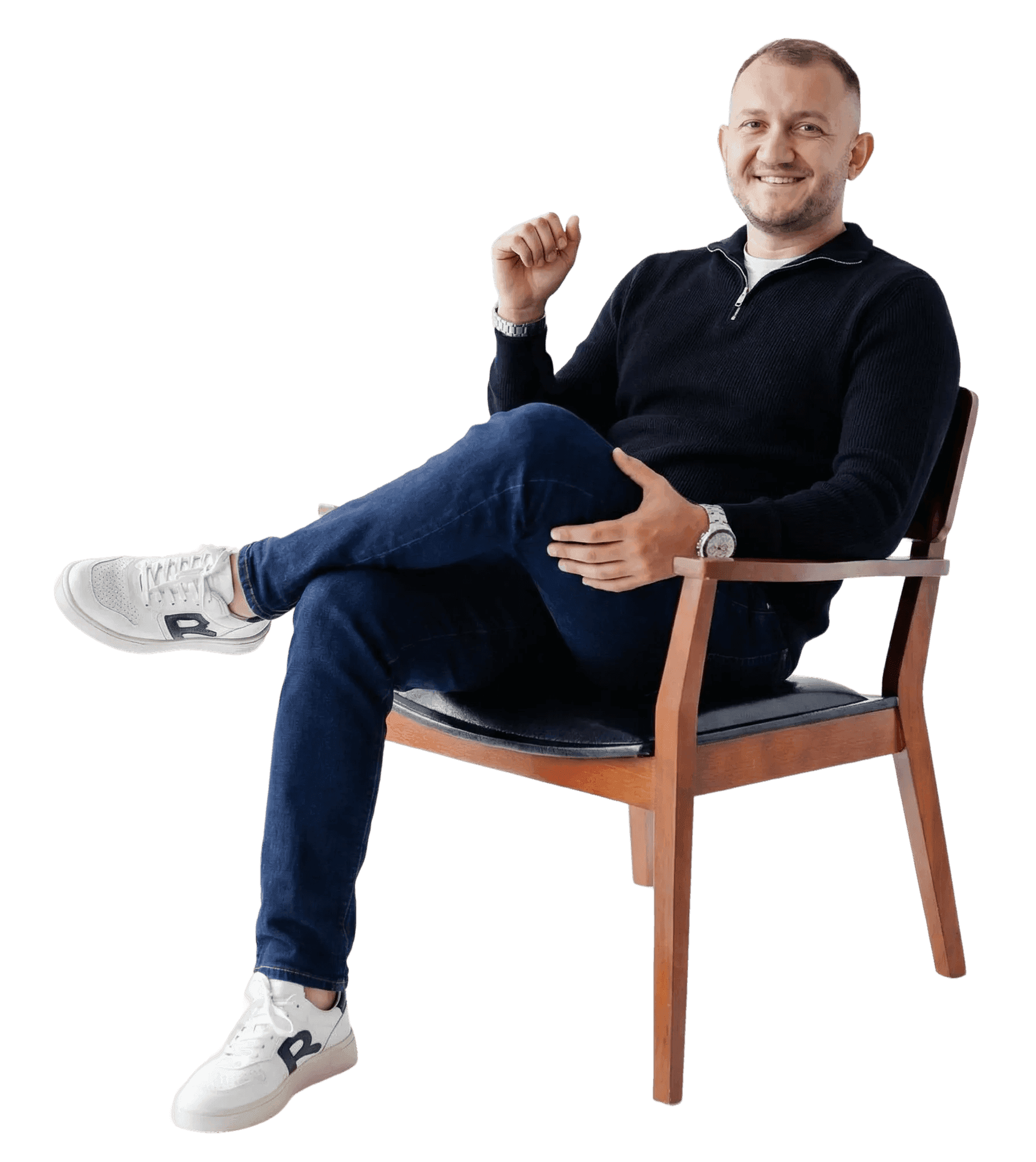 Senior UX designer sitting on a wooden chair with crossed legs, photographed against a clean background, conveying a calm and thoughtful professional presence.
