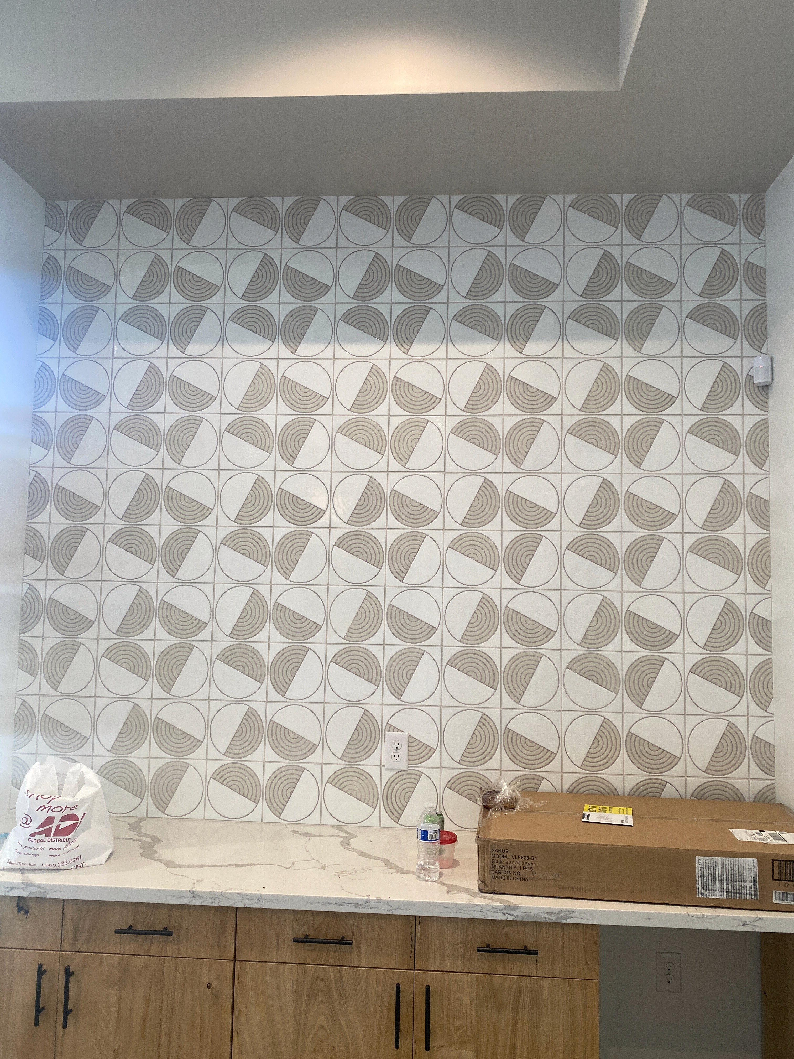 Geometric patterned wall tiles in white and gray installed in a recessed niche above a marble counter, under construction.