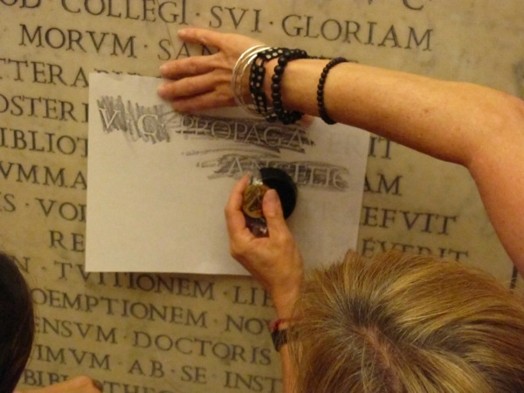 A person copying on a piece of paper some engraved writings from a wall.