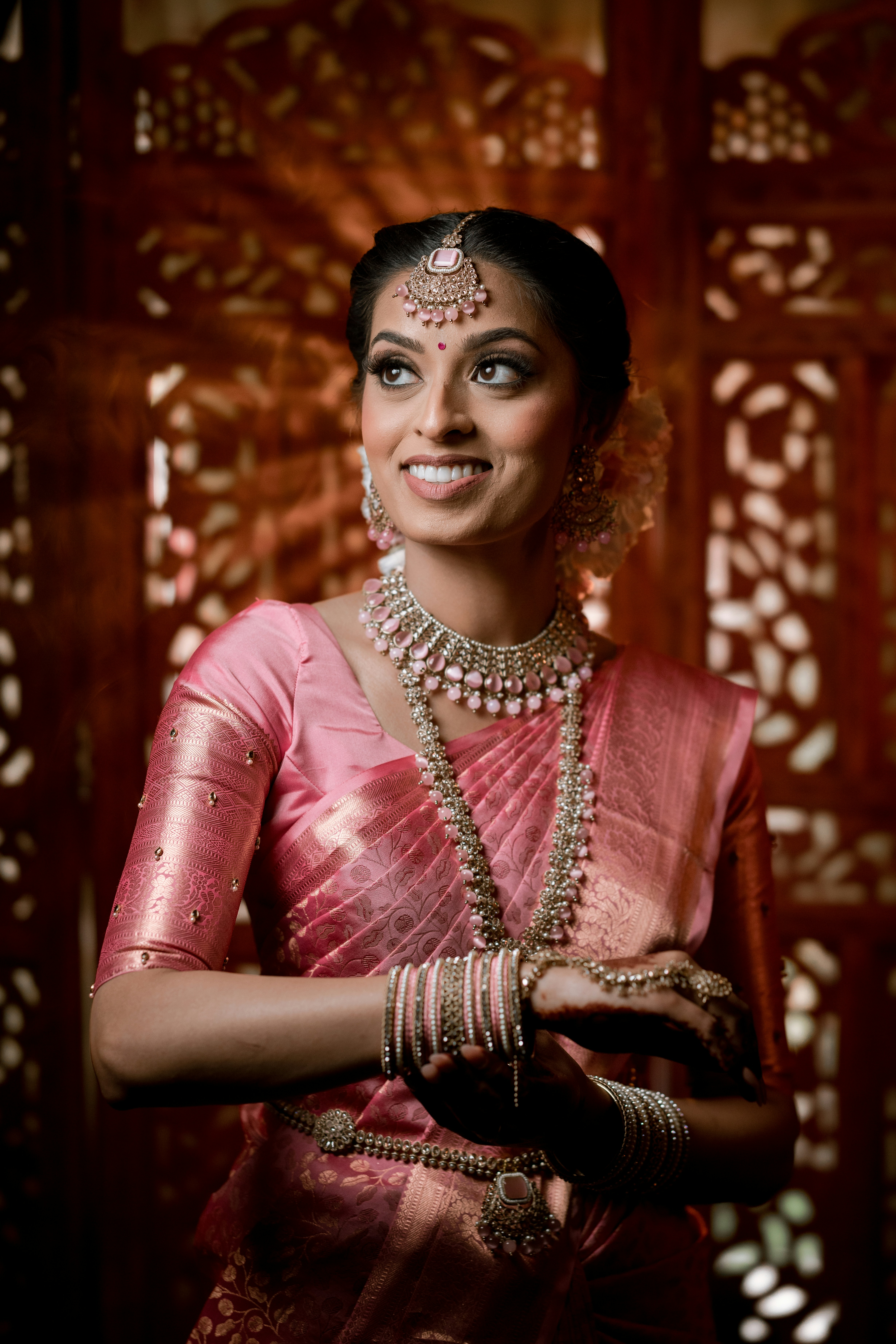 A smiling woman in a pink sari and jewelry.