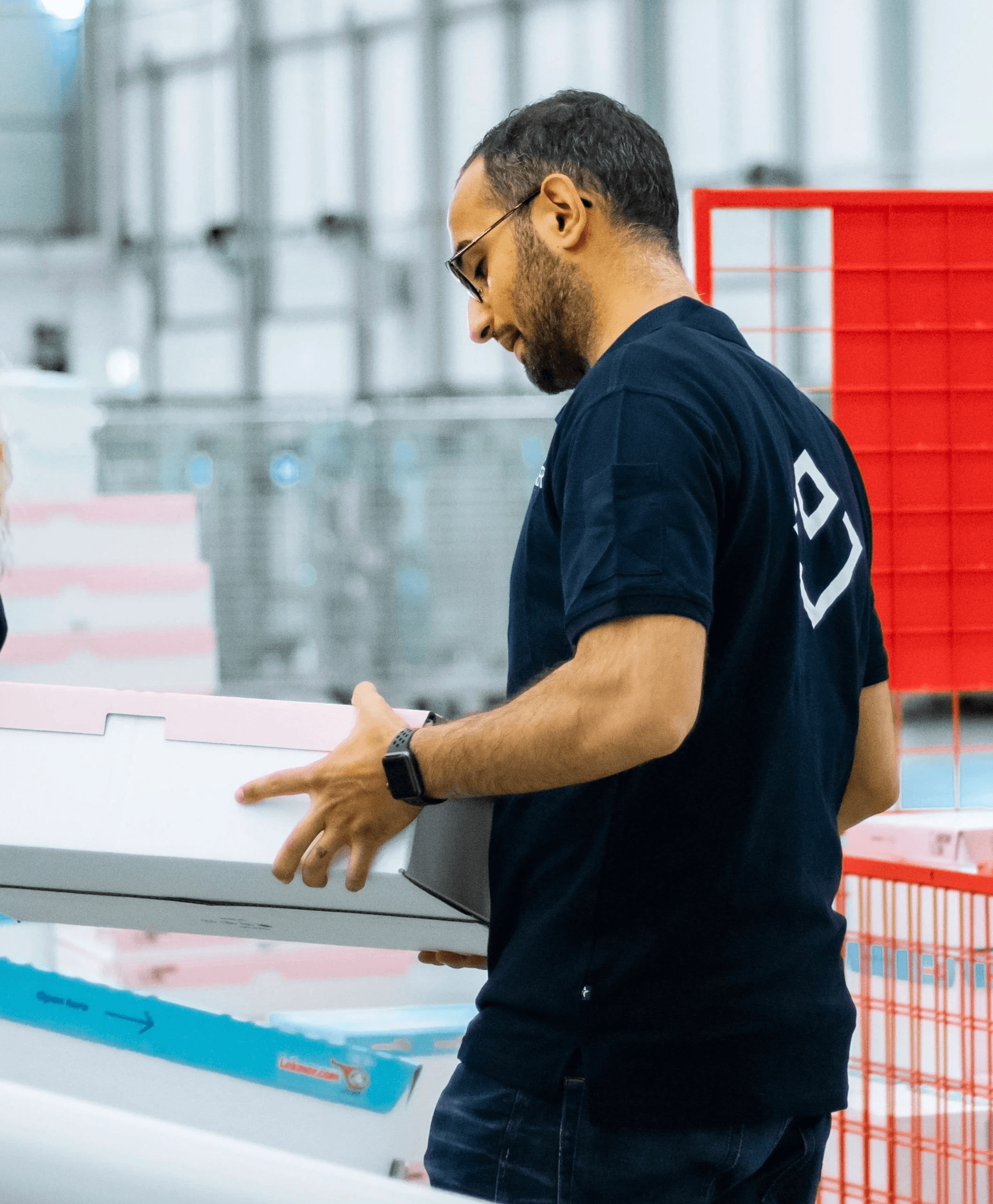 A man in a dark sweater and a woman in glasses wearing a navy blouse sit together at a desk, smiling at the camera with a laptop in front of them.
