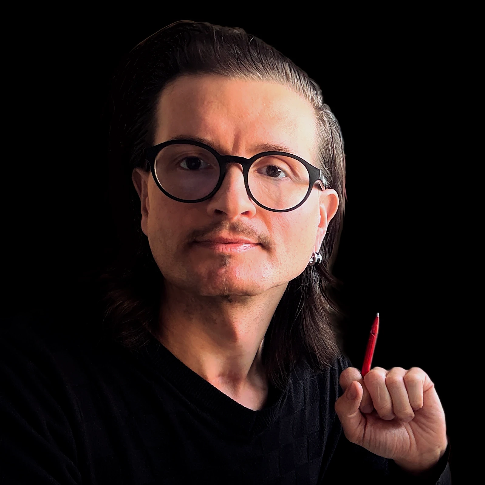 Professionelles Porträt von Jens Pfeifer mit runder schwarzer Brille und langen, dunklen, zurückgekämmten Haaren vor schwarzem Hintergrund, der einen roten Stift hält und ruhig in die Kamera blickt.