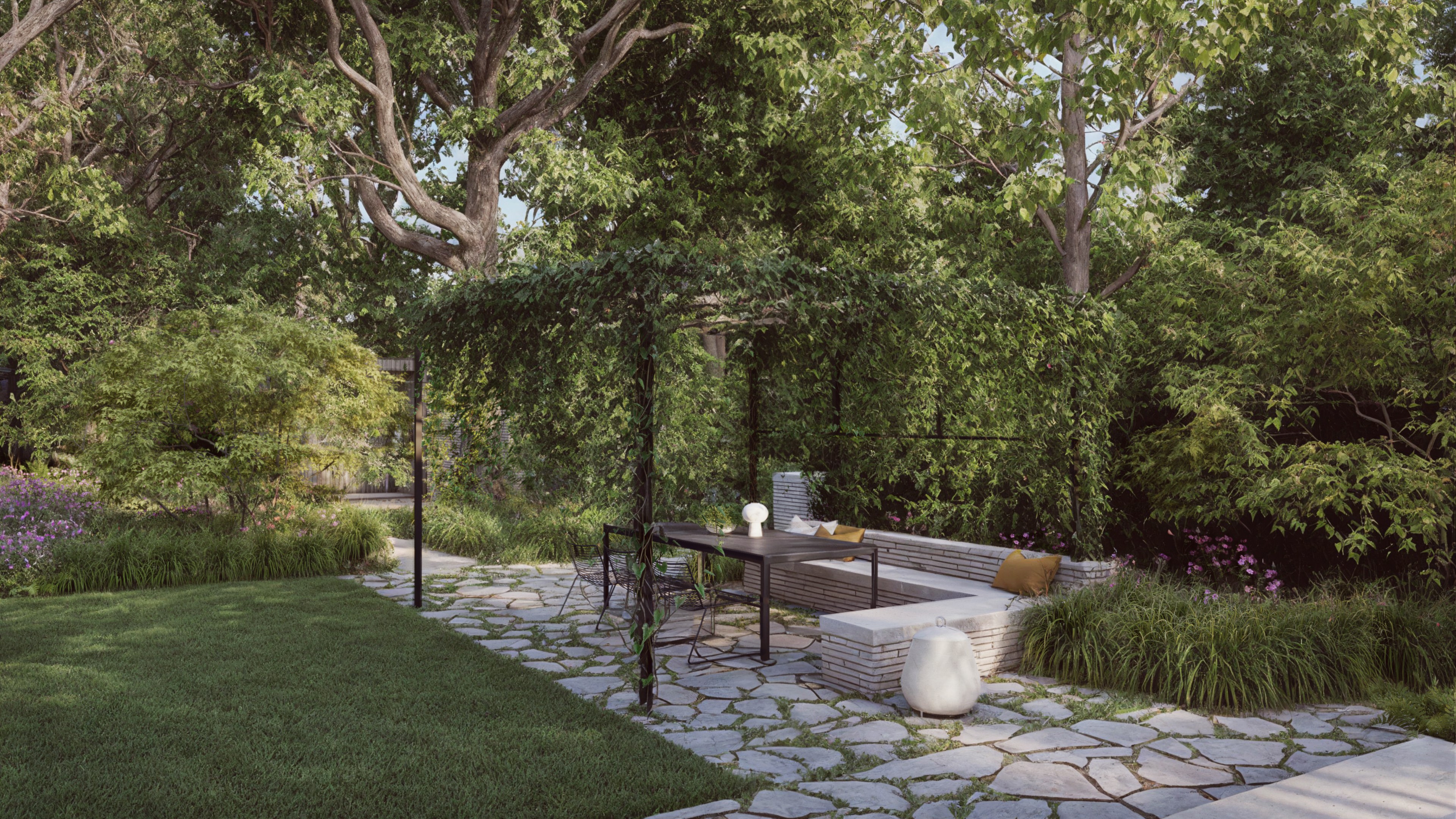 A stone patio with a dining table and bench under a leafy pergola in a lush, green backyard.