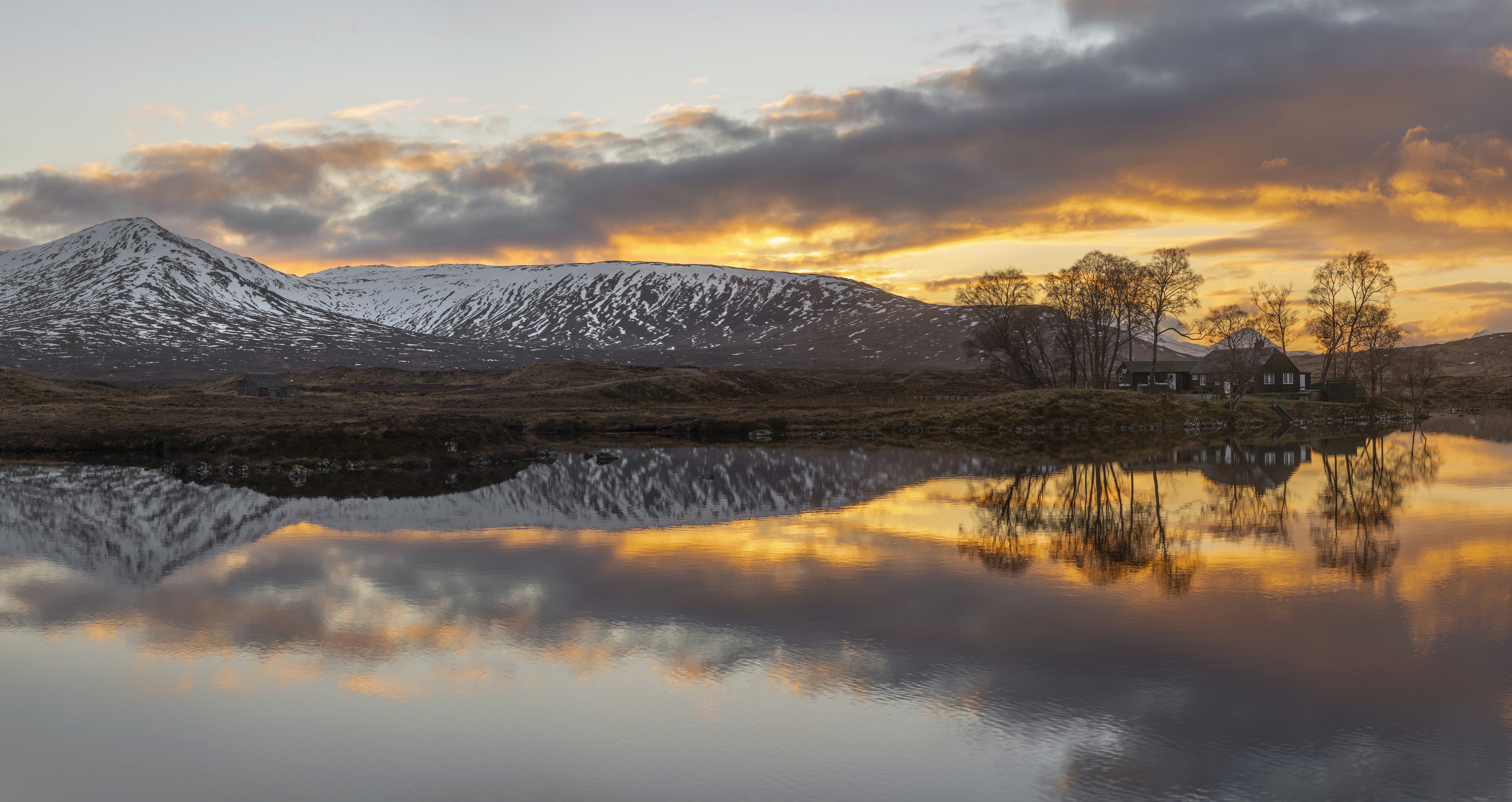 SSunrise on the water with snow-capped mountains in the background and Loch Ossian Youth Hostel at the water's edge