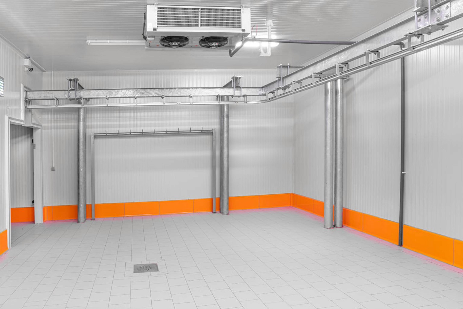 Innenansicht eines modernen Industriekühlraums mit installierter Decken-Kühleinheit und einem verzweigten System aus Rohrleitungen und Kabeltrassen an der Decke. Die sterile, helle Umgebung verdeutlicht die professionelle Installation großgewerblicher Kältetechnik.