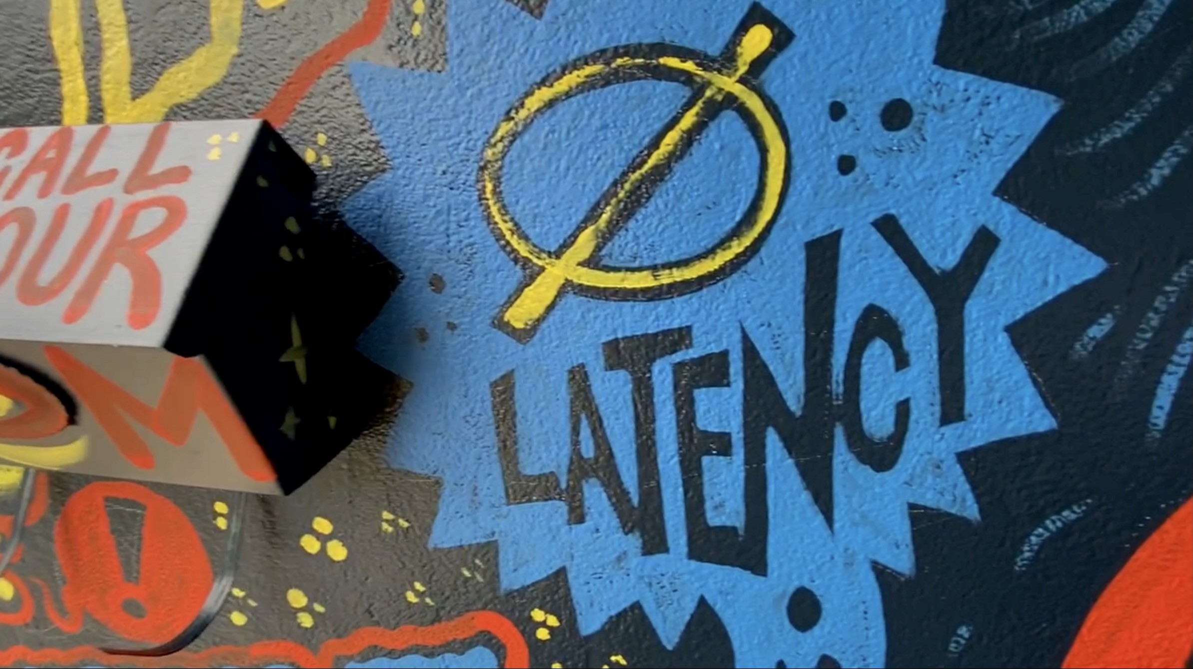 Close-up of the word “Latency” painted in black on a blue burst beside an empty-set symbol.