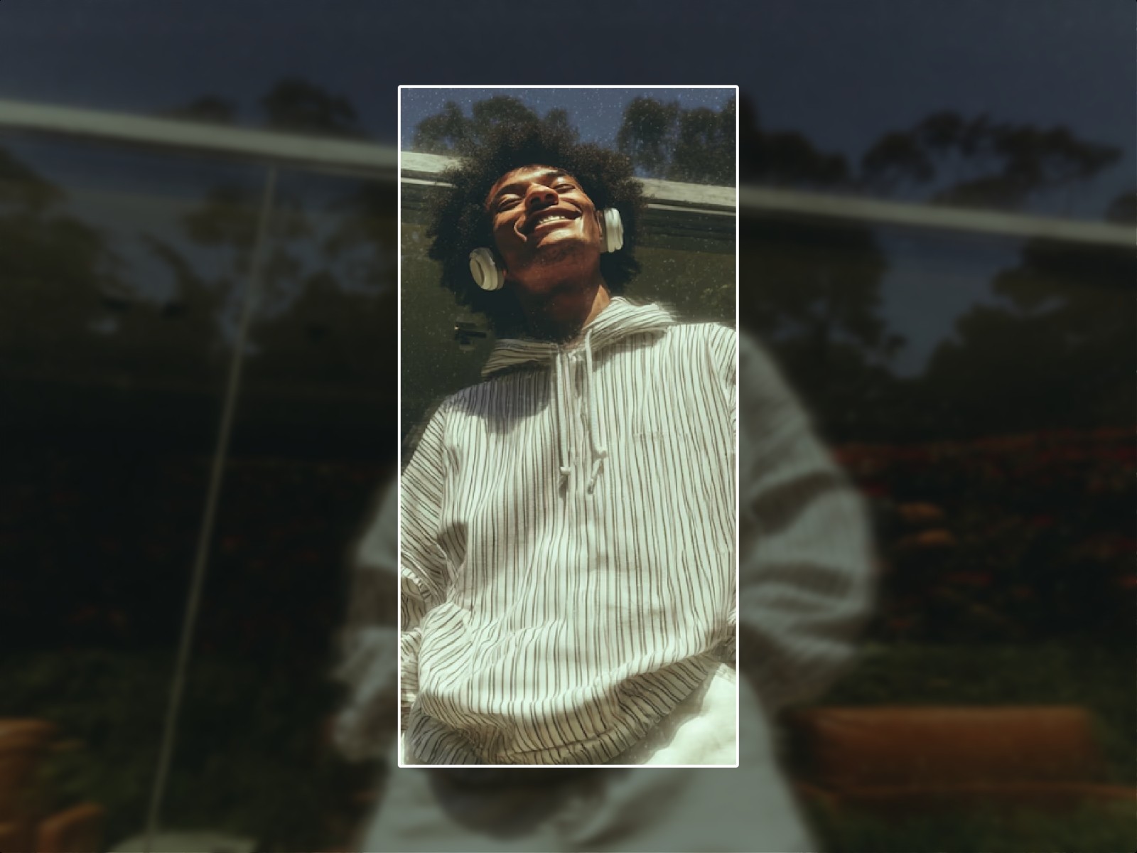 Portrait of a smiling young man with headphones, shown in a vertical frame over a blurred background of the same image.