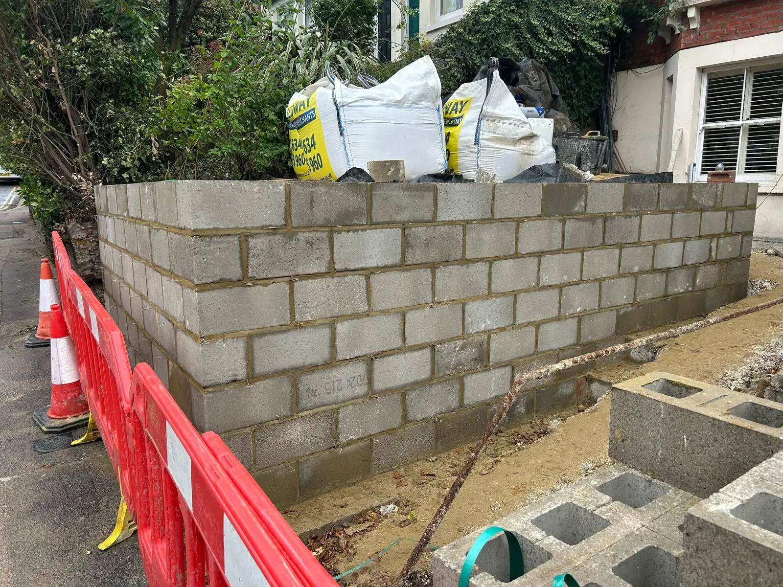 Construction site with a partially built concrete block wall and safety barriers in the foreground.