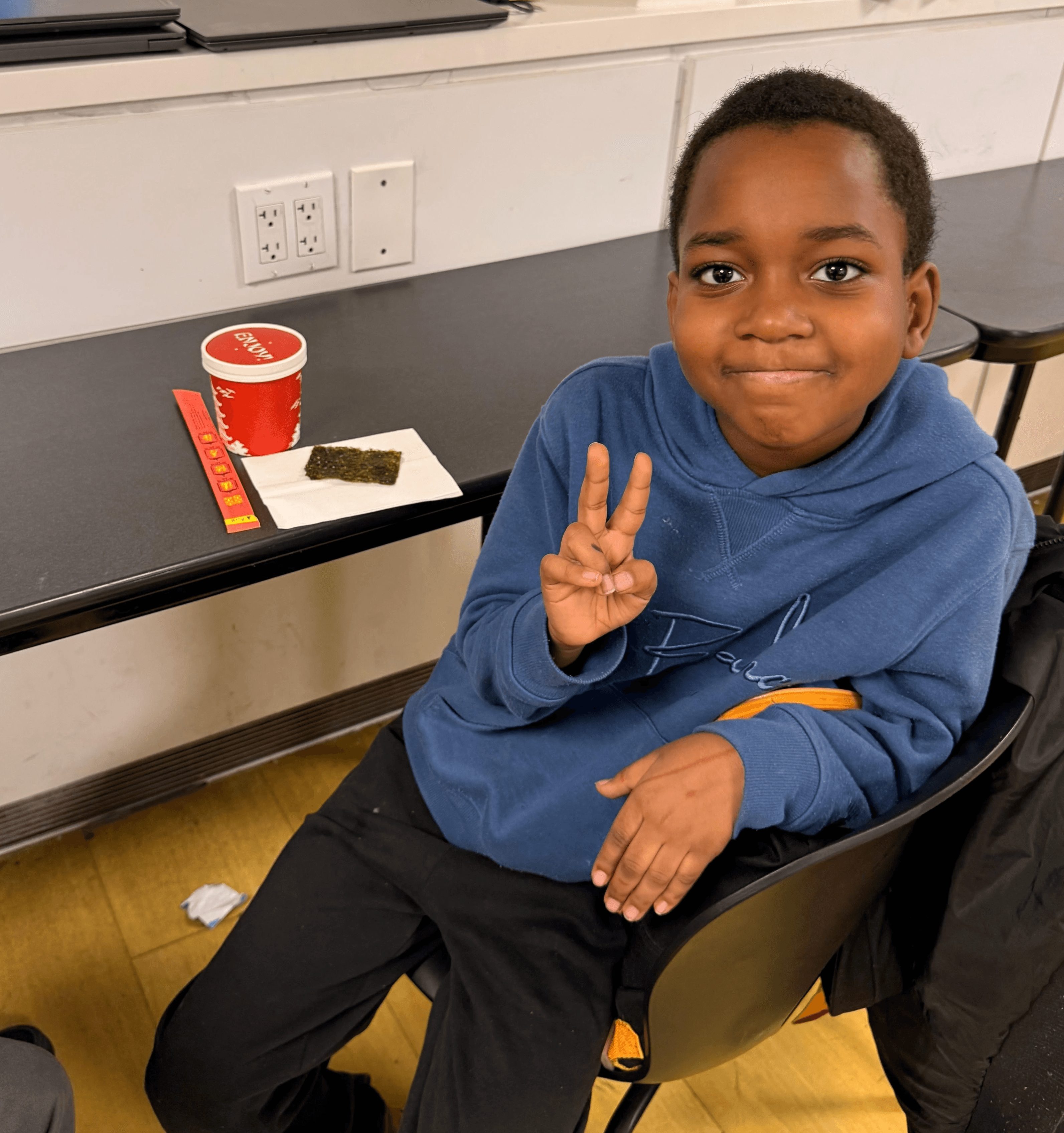 Participant flashes a peace sign with his ramen, chopsticks, and seaweed snacks.