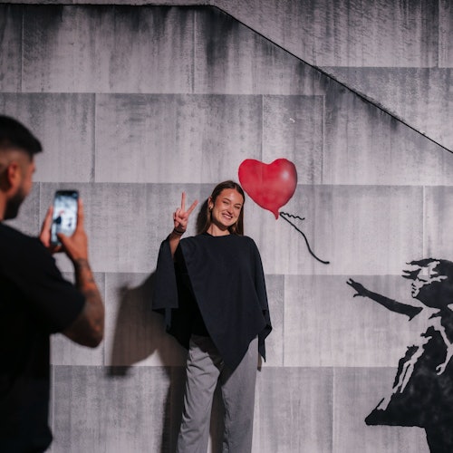 Dziewczyna pozuje obok jednego z muralów Banksy'ego na wystawie.