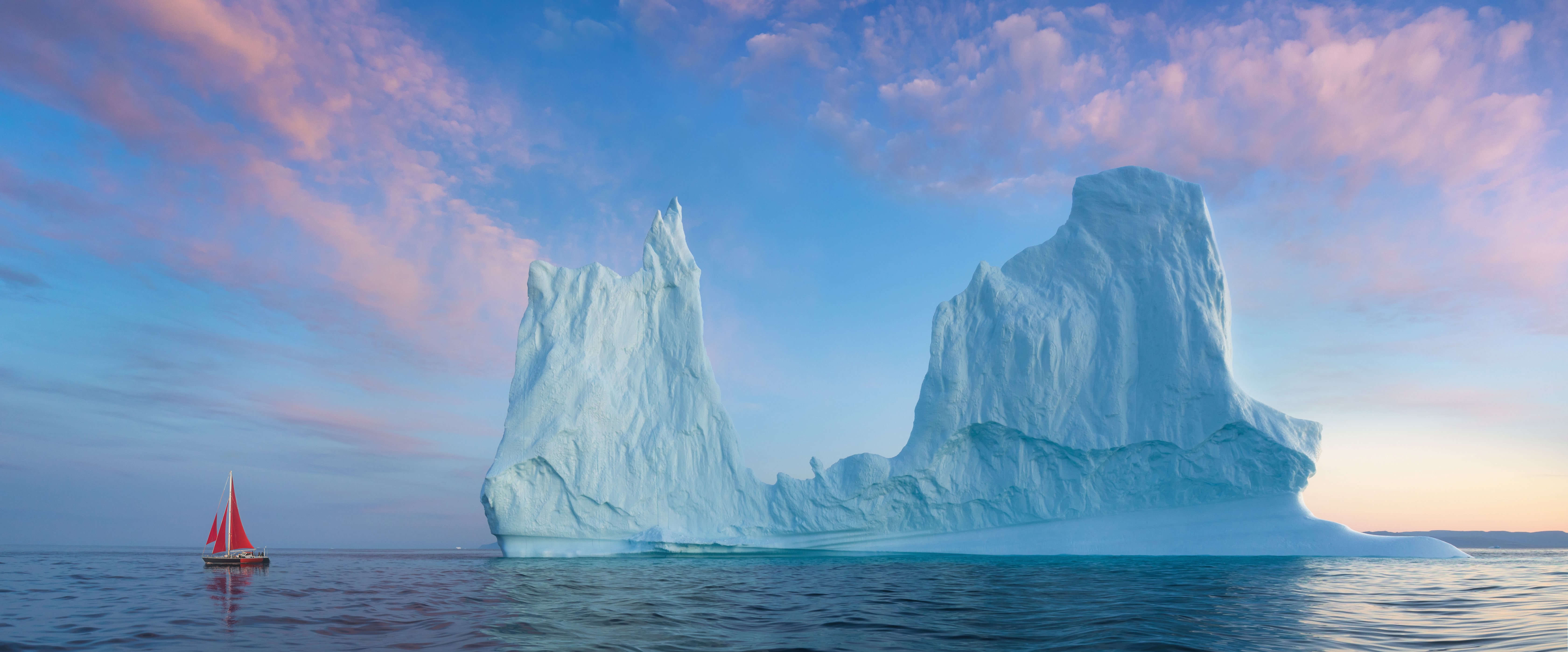 Voilier rouge naviguant à proximité d’un grand iceberg.