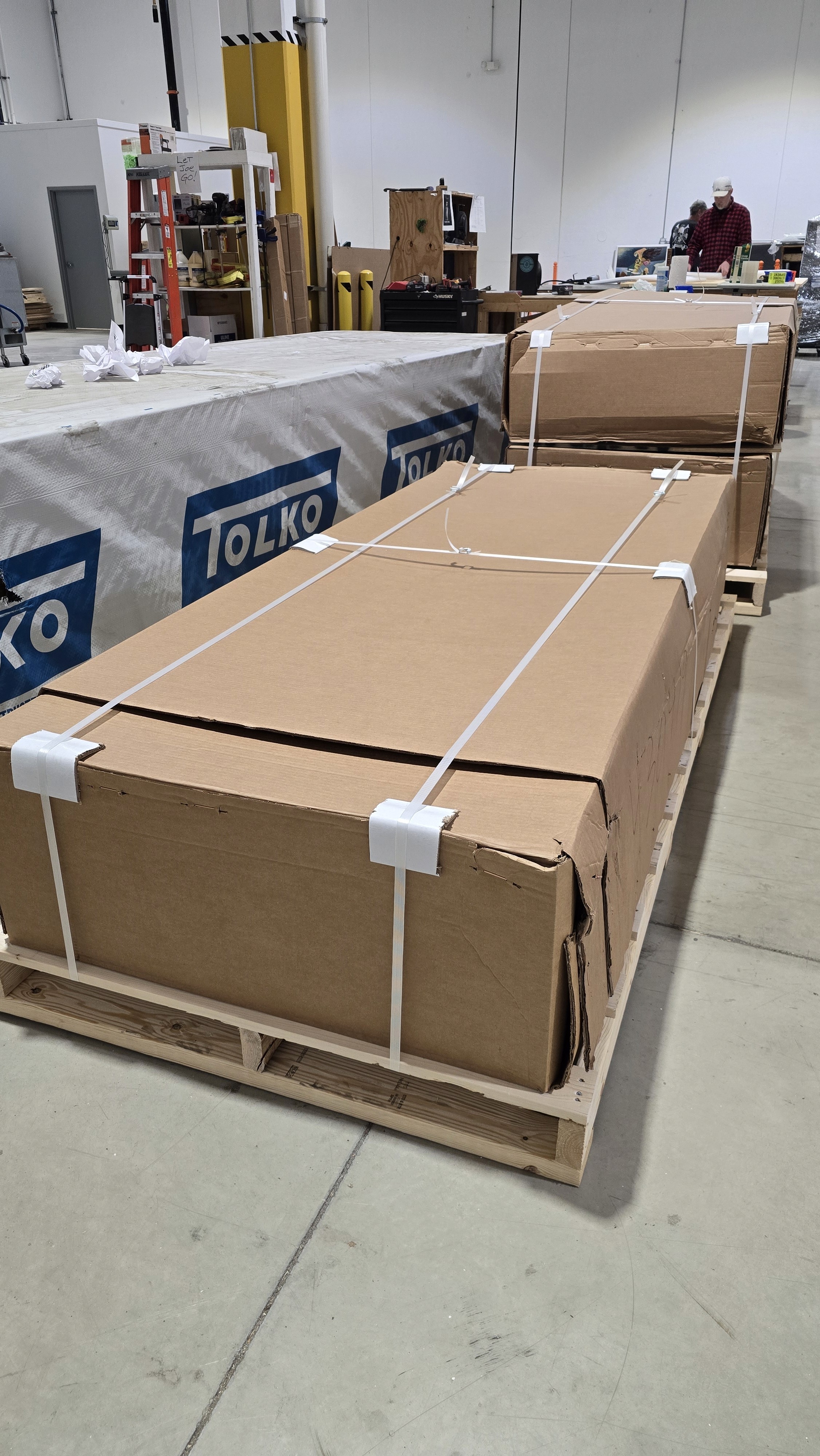 A young person with curly hair smiles at the camera while sitting in front of a laptop against a dark background.