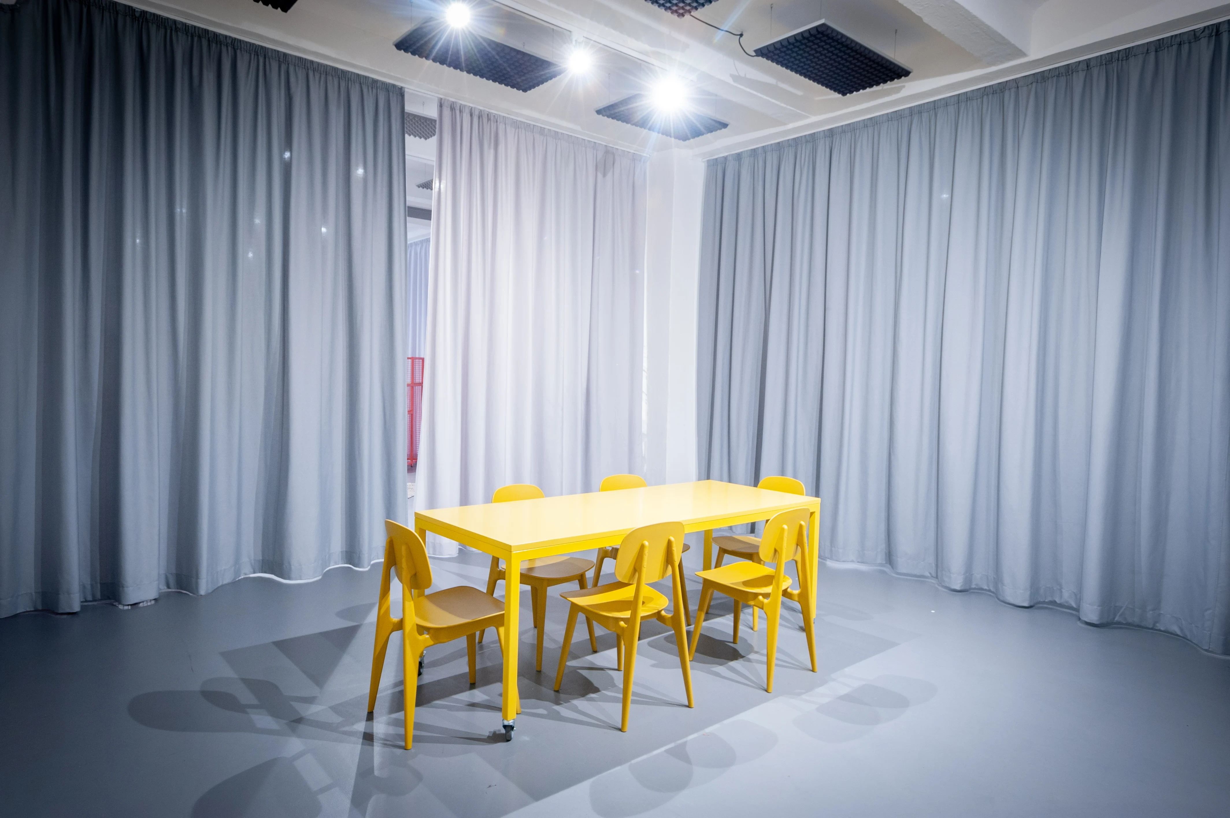 Meeting space at HEY CONTENT STUDIO with a bright yellow table and chairs on a grey floor, enclosed by floor-length grey curtains.