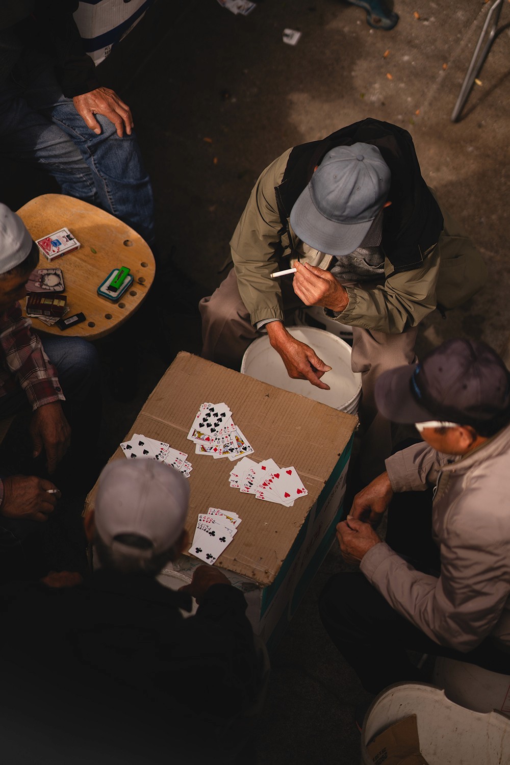 Men in hats playing cards in chinatown while smoking.