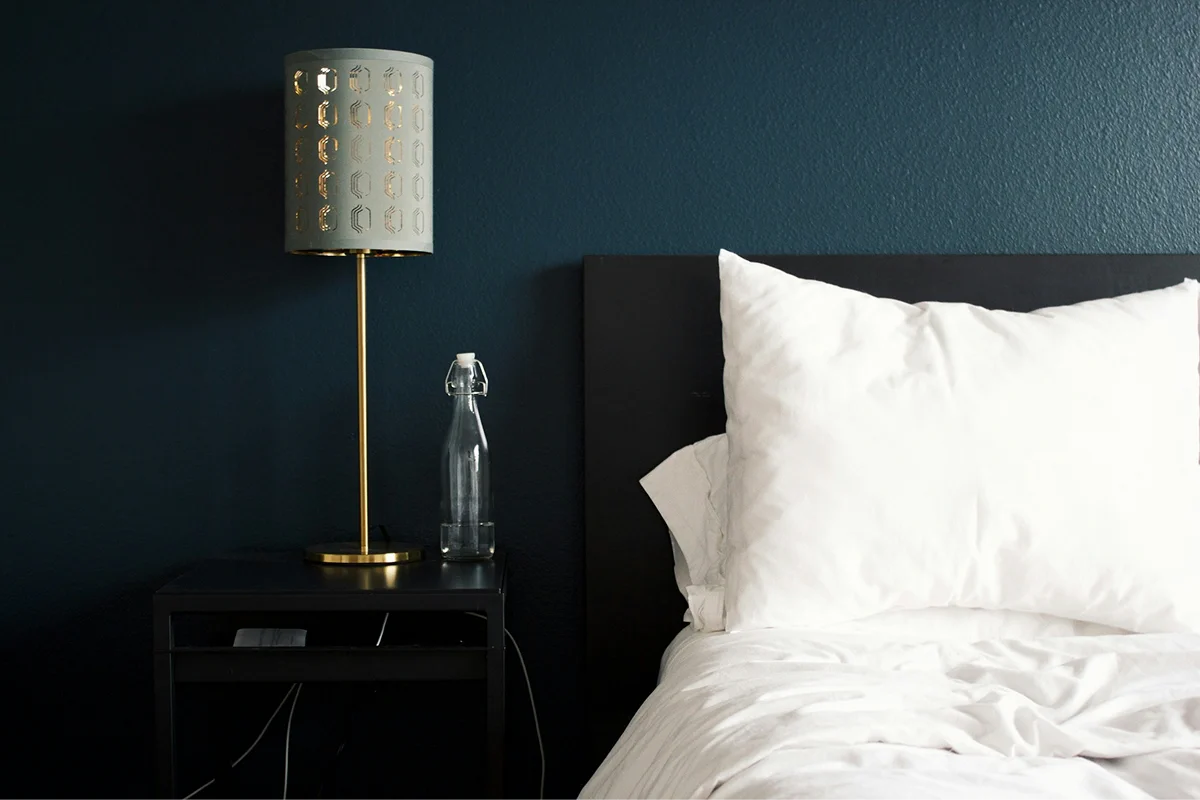 King bed with bedside lamp against a dark green wall.