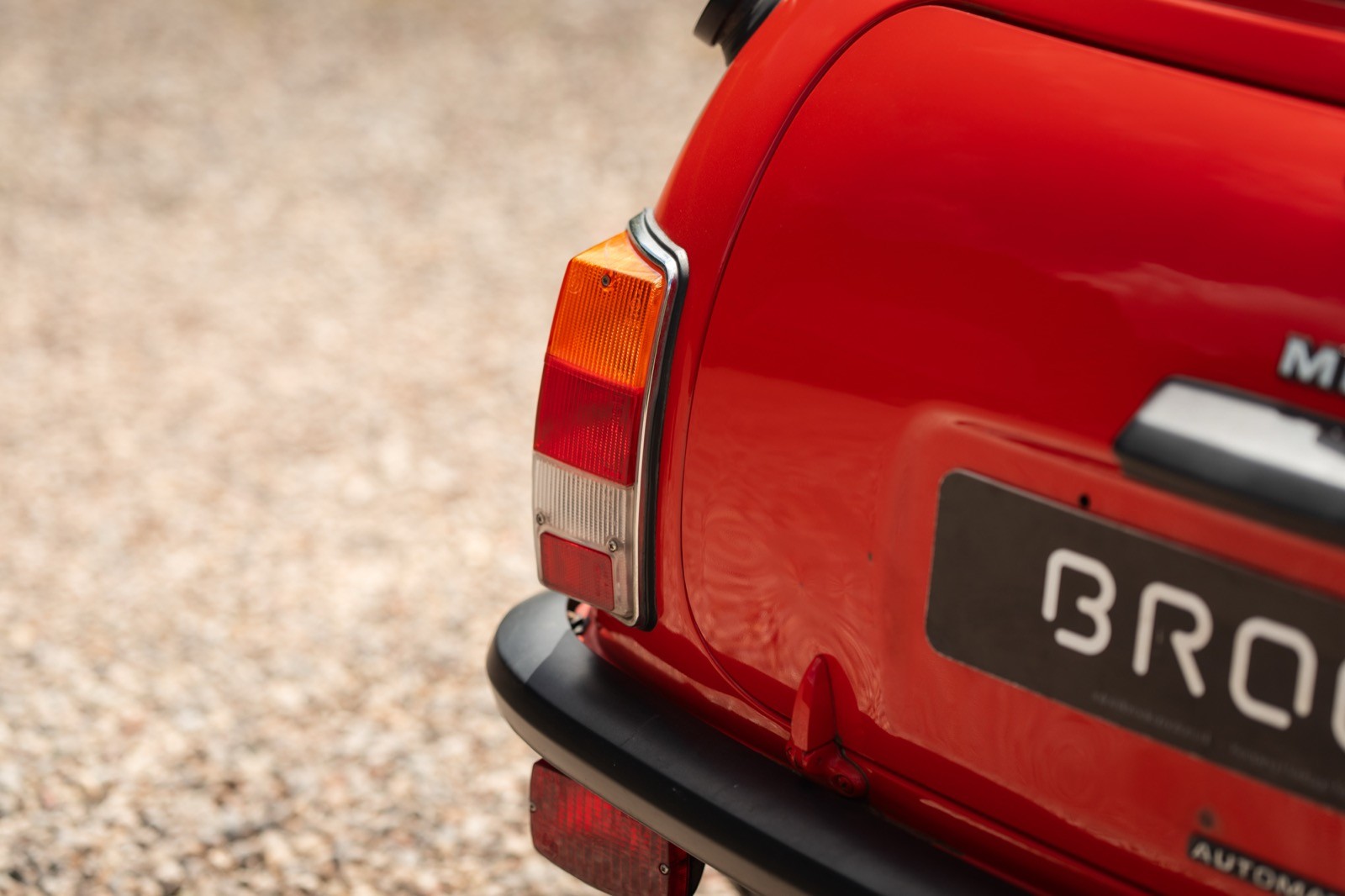 Close-up of the rear of a bright red vintage car parked on a gravel surface.