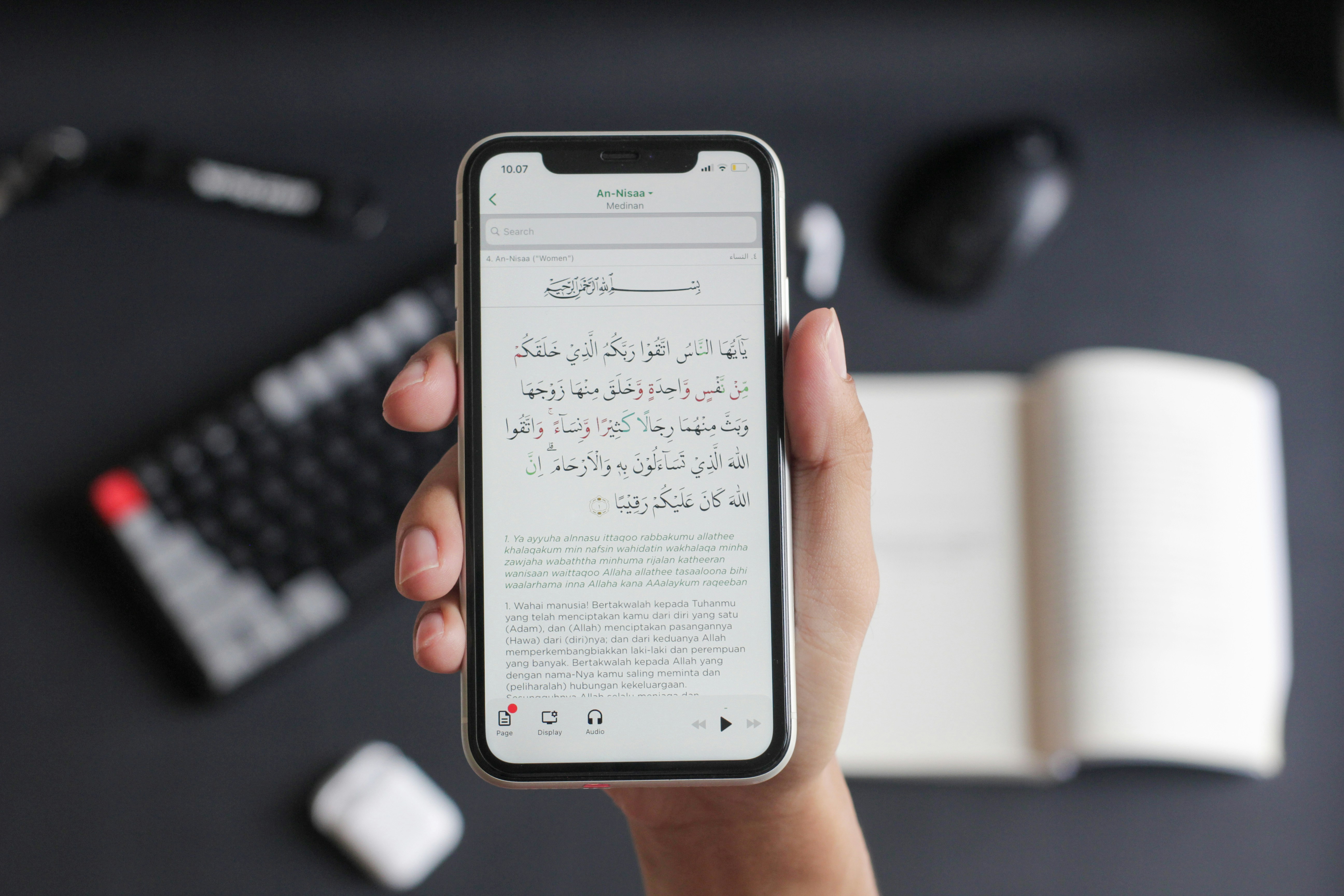 A hand holding a smartphone displaying a Quran app