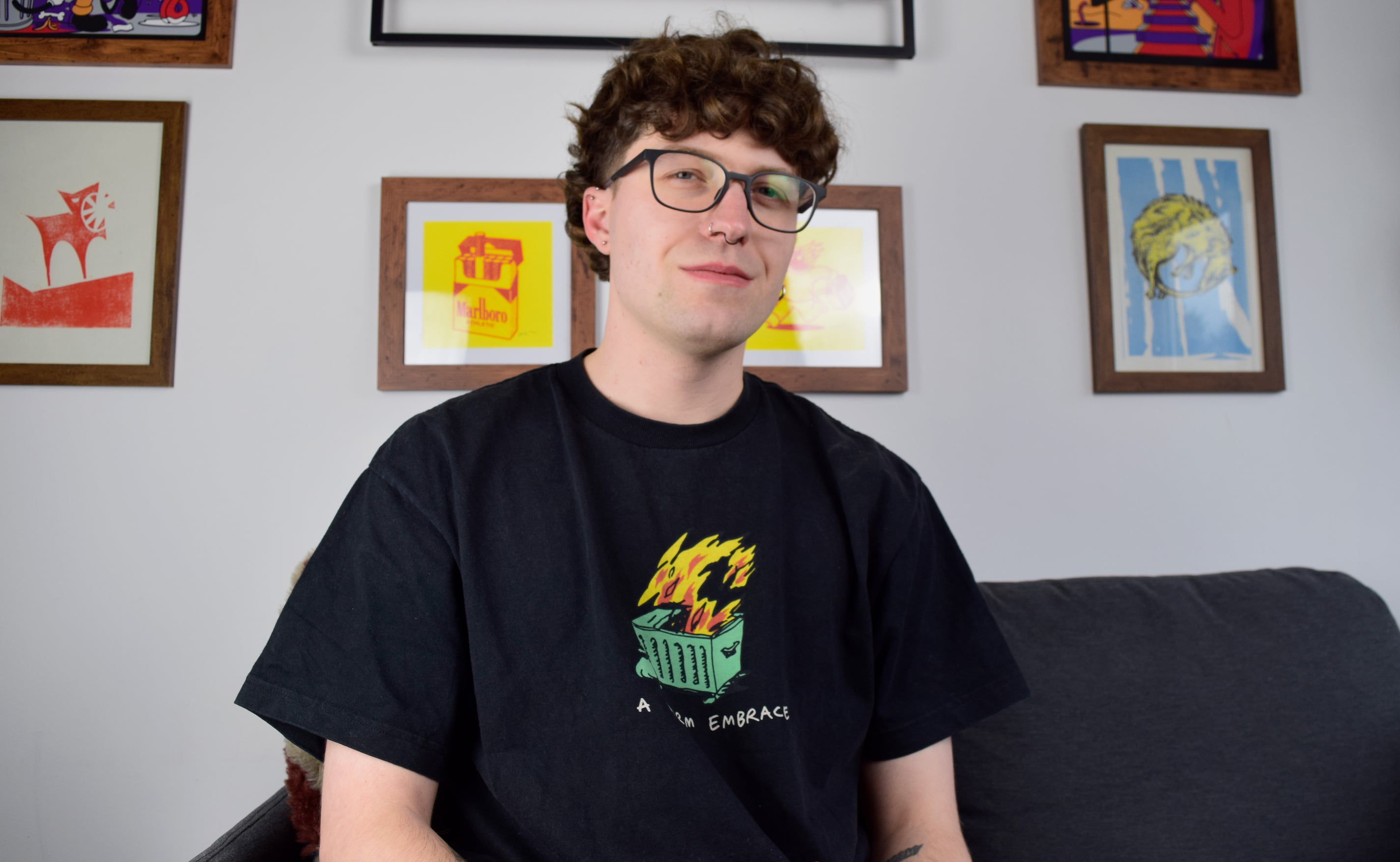 Graphic design freelancer in glasses and a black t-shirt, seated on a sofa in an office.