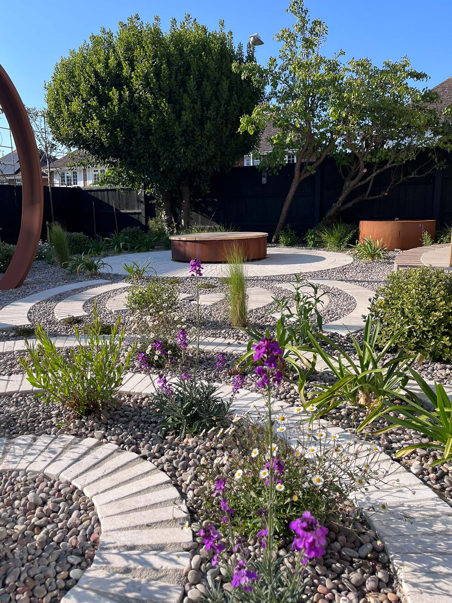 A serene garden path winds through vibrant flowers and lush greenery under a bright blue sky.