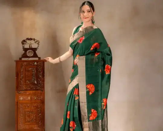 A woman wearing a green Dupion silk saree from That Saree Shop, featuring elegant golden borders and delicate orange floral prints, blending textured luxury with vibrant handcrafted detail.