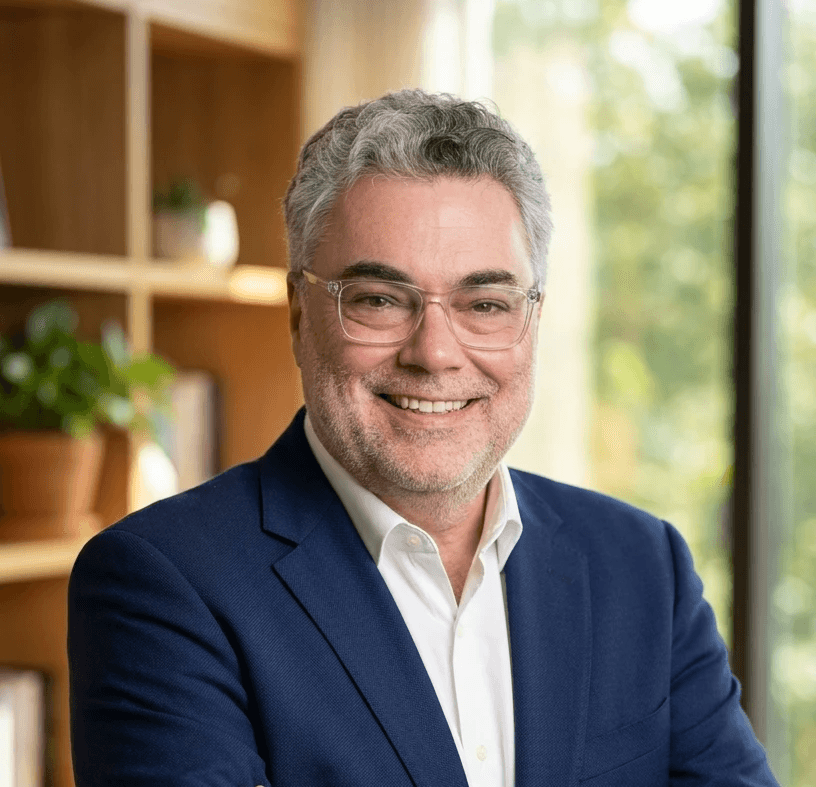 Smiling young woman with curly hair sitting at a laptop, in front of a teal wall.