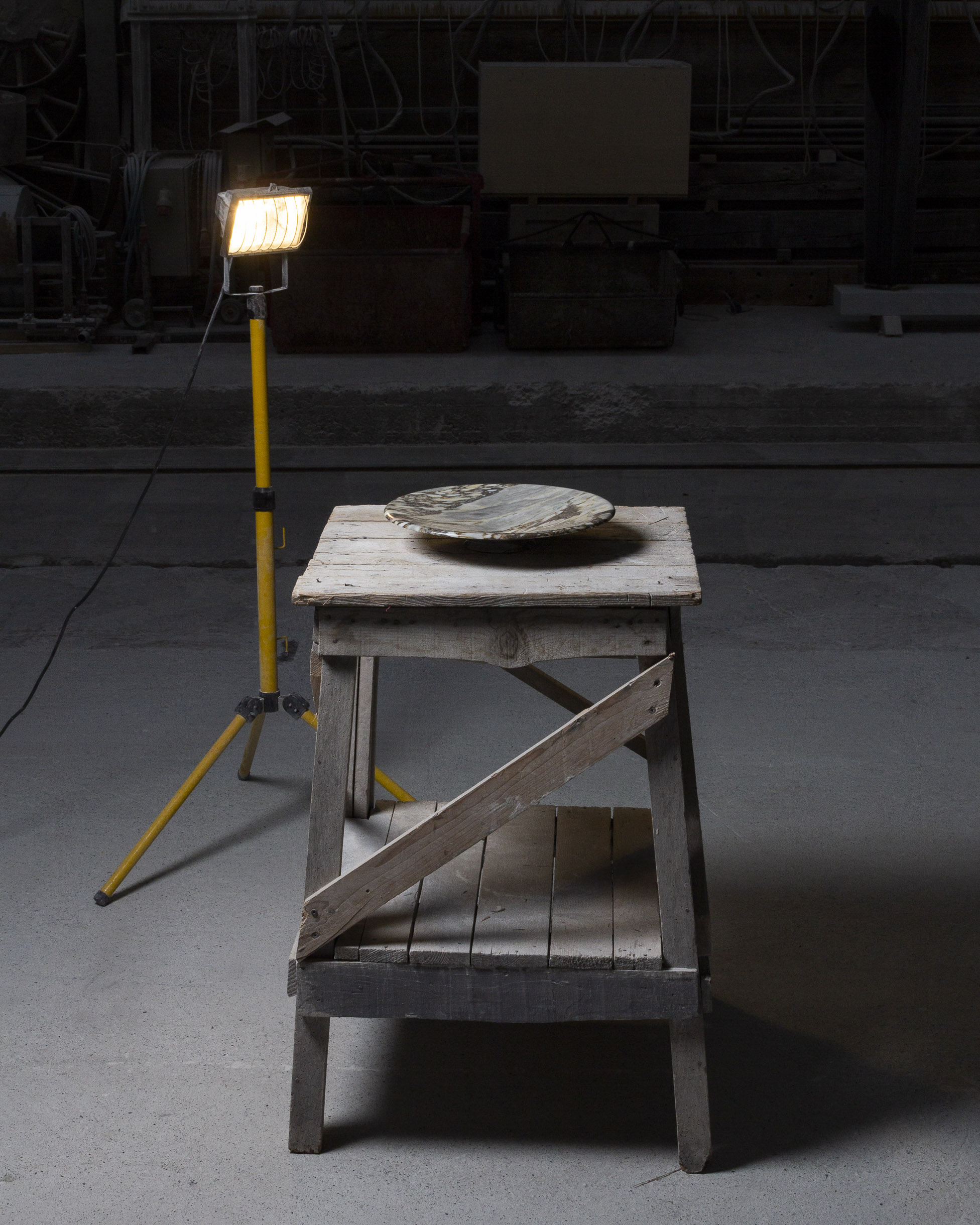 Mise en scène d'un bol en marbre rare posé sur une table en bois et éclairé par une lampe de chantier