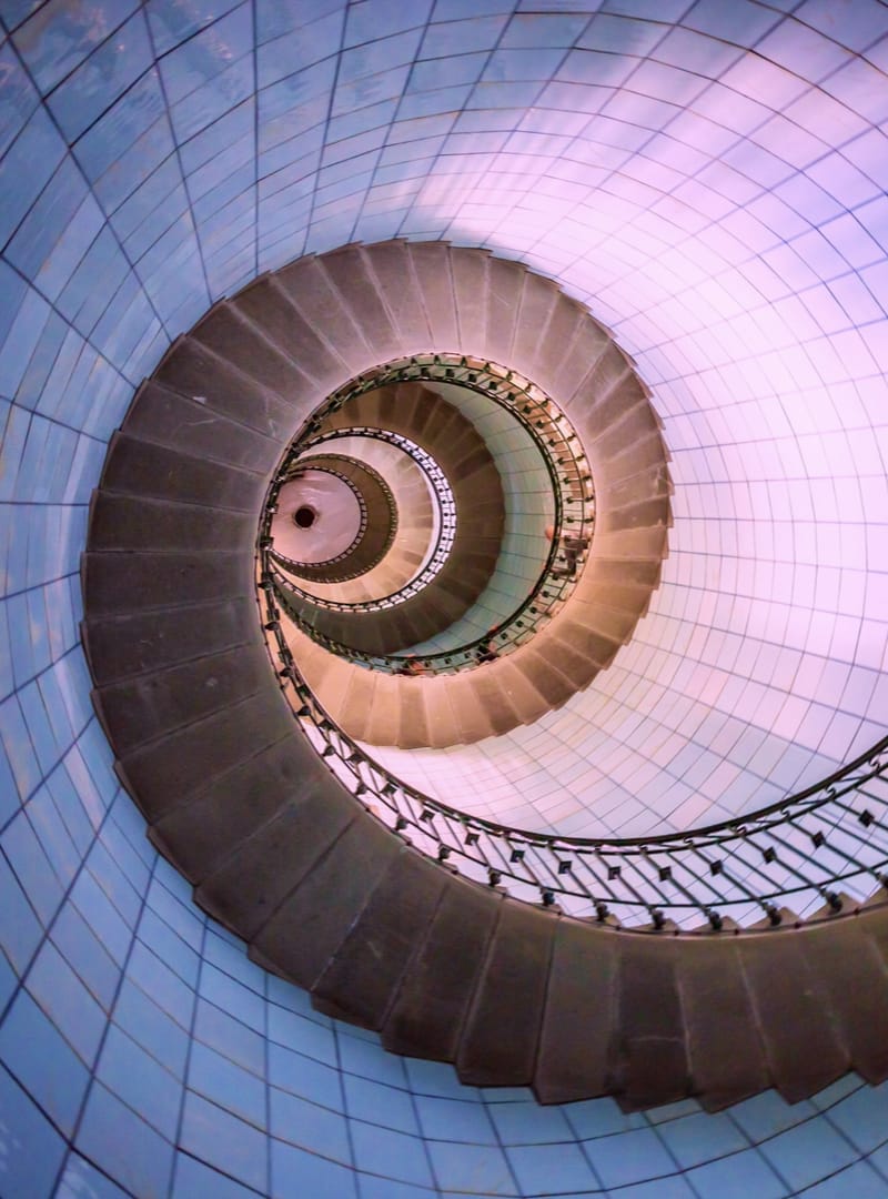 A photo of a spiral staircase in a lighthouse from below, representing many steps leading to higher ground