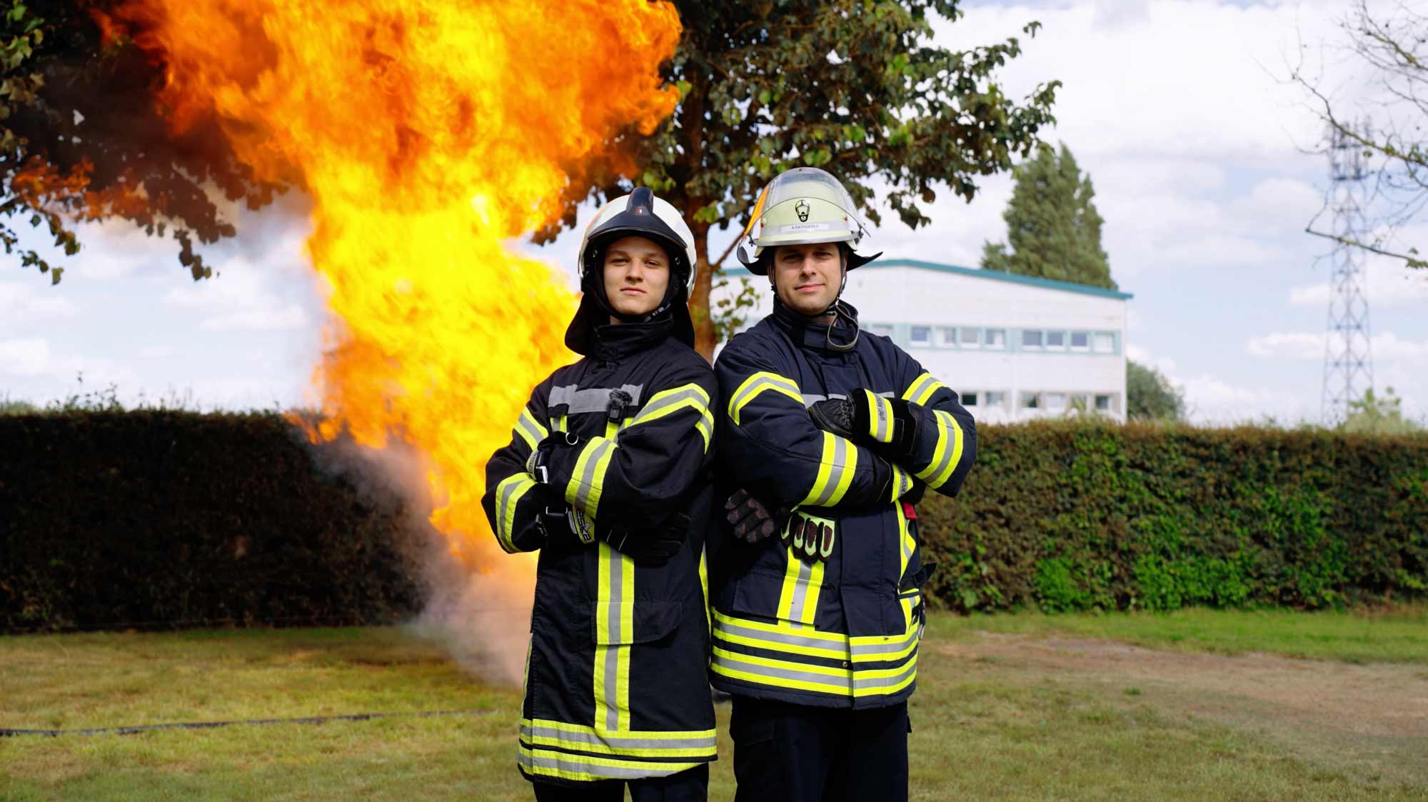 Firefighters poised for action; flames blaze behind. Filmproduction for a strategic brand campaign in advertising and storytelling.