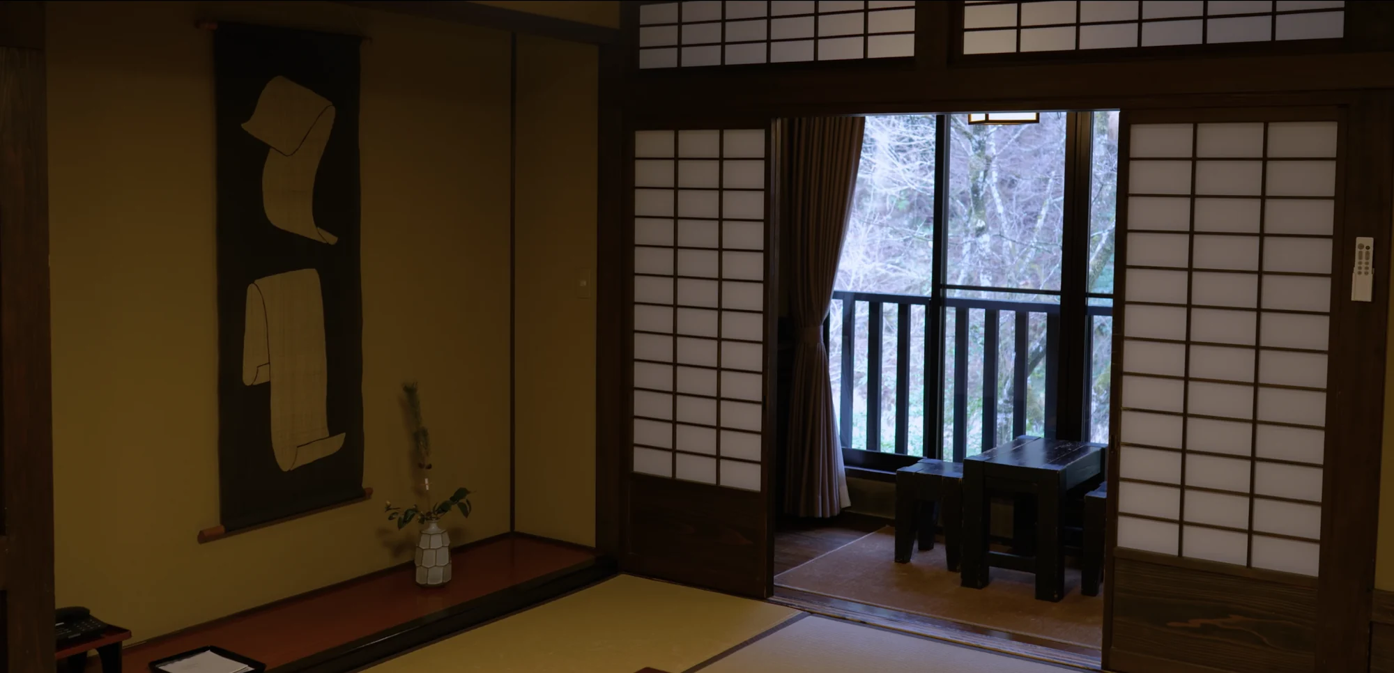 A tatami guest room with scroll and flower in the alcove and shoji open to a balcony