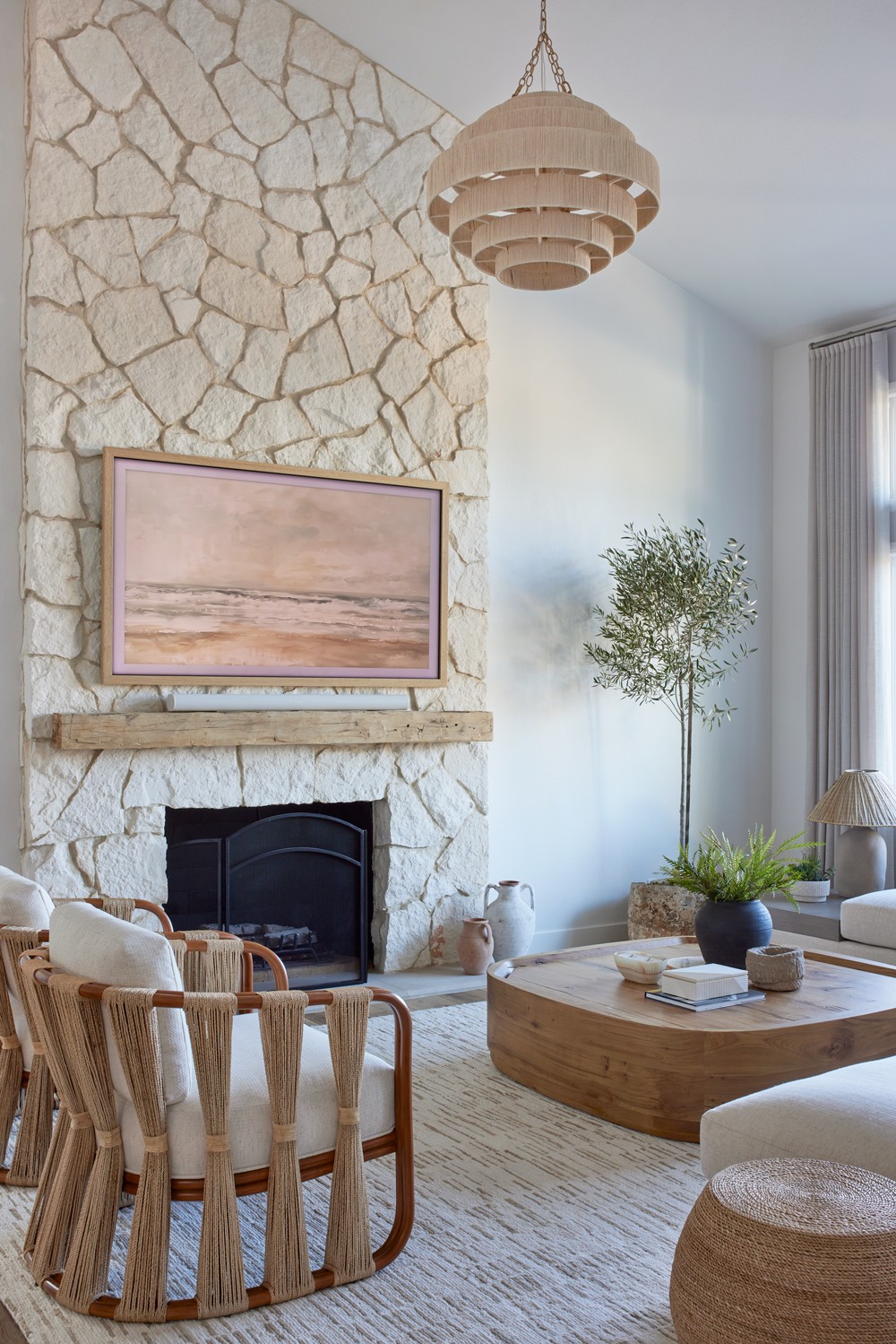 This luxurious interior features a limestone fireplace, timber accents, woven wooden chairs, and a natural wood coffee table, all unified by an earthy tonal palette