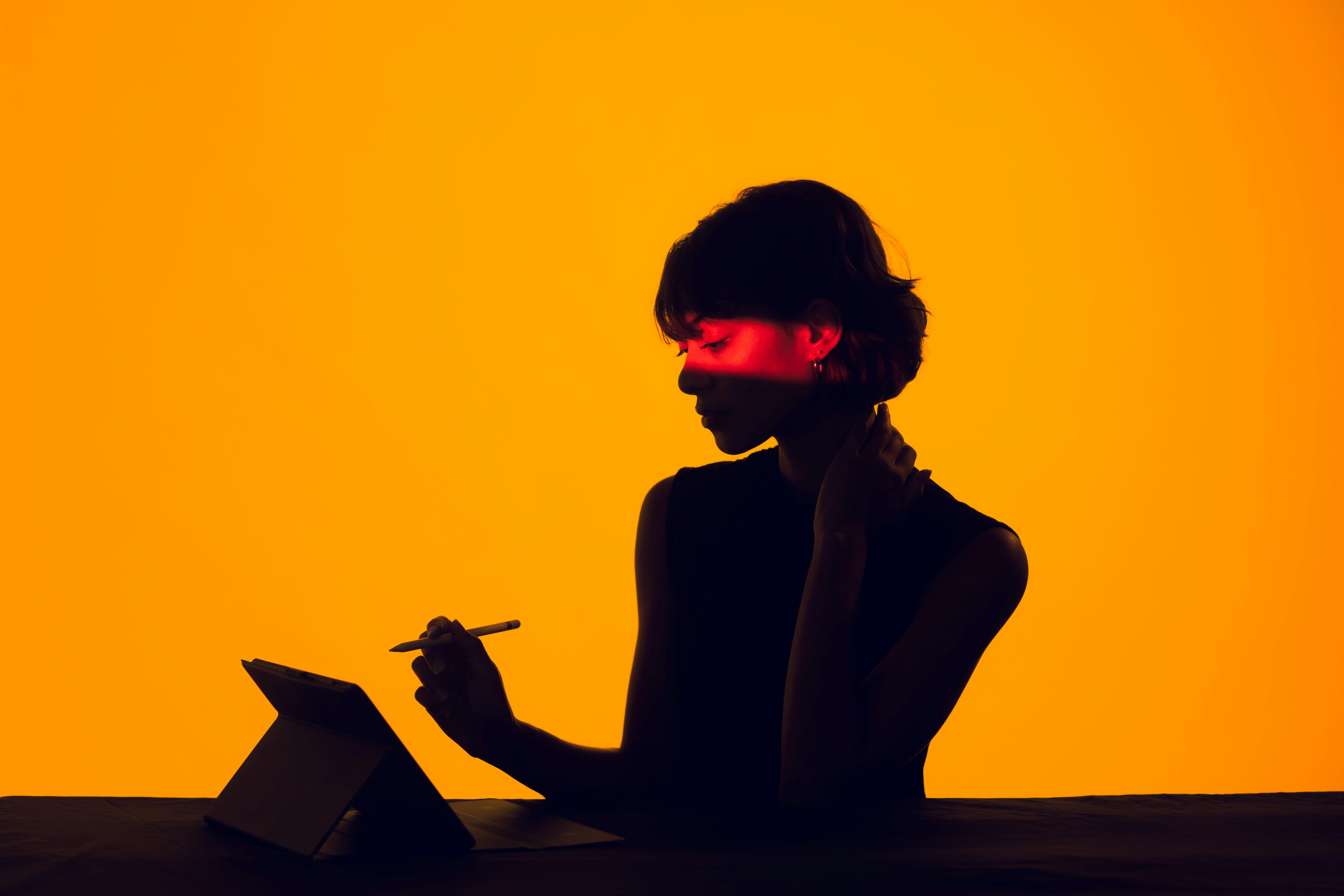 Silhouette einer Person, die mit Stift an einem Tablet arbeitet, vor orangefarbenem Hintergrund – Symbol für kreative Umsetzung und digitales Schaffen.