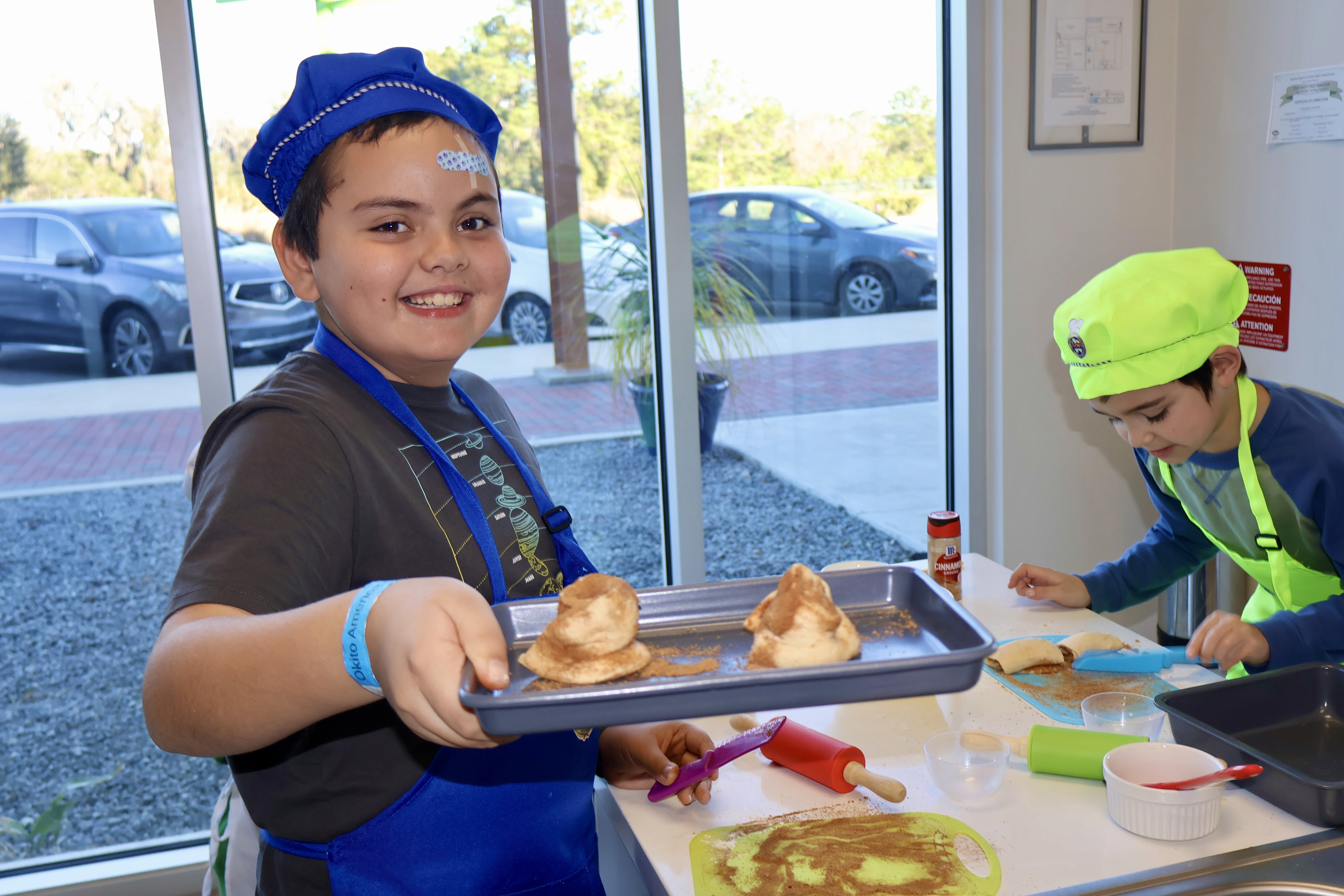 A smiling child holding up a tray with cinnamun rolls ready to bake