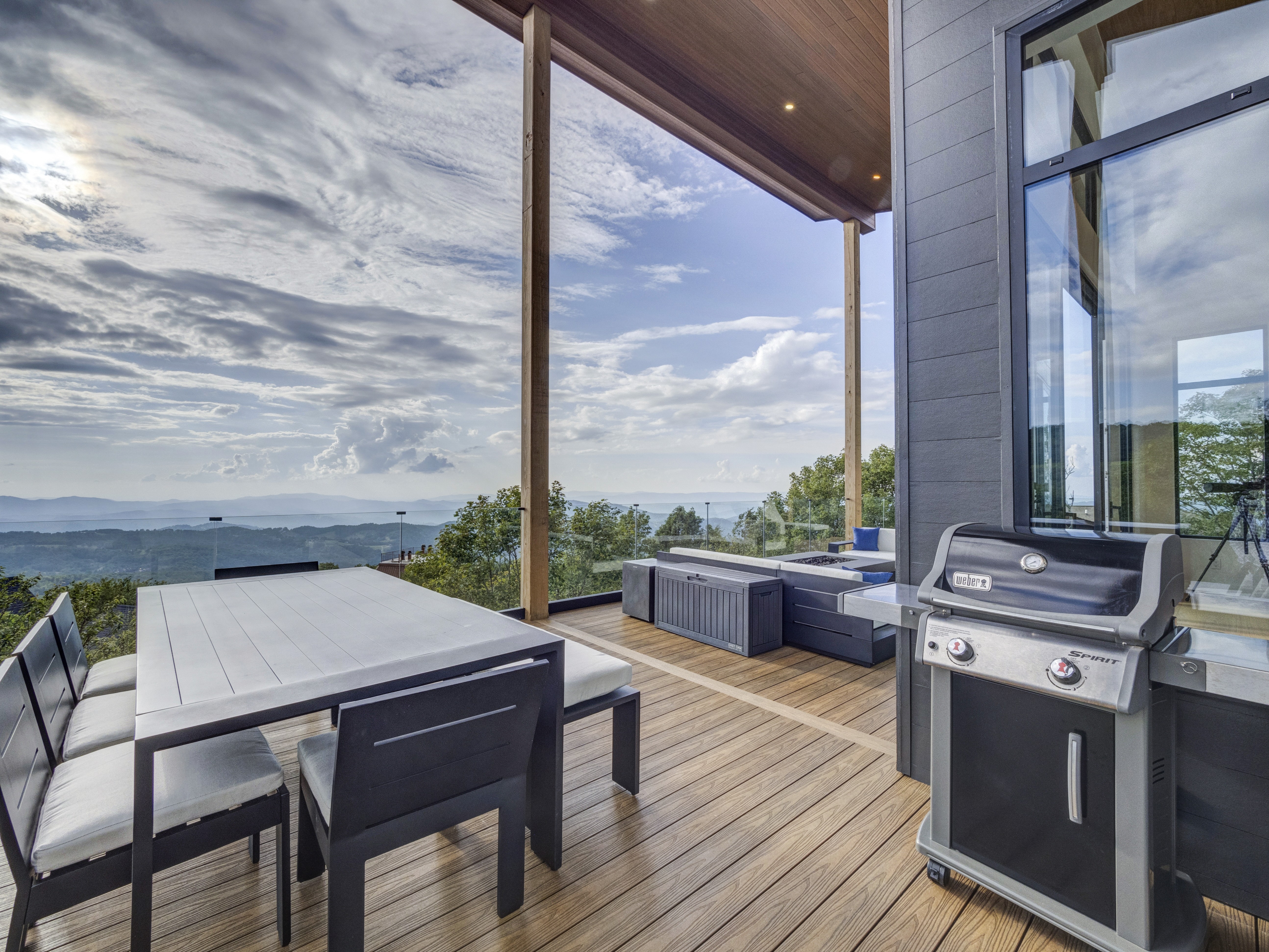 Modern outdoor kitchen setup featuring a stainless steel grill and dining area on a luxury deck with mountain views