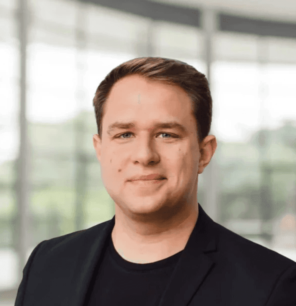 Enrico Bernardo, Geschäftsführer der hellomed Group GmbH, Portrait eines Mannes im schwarzen Sakko vor moderner Glasarchitektur.