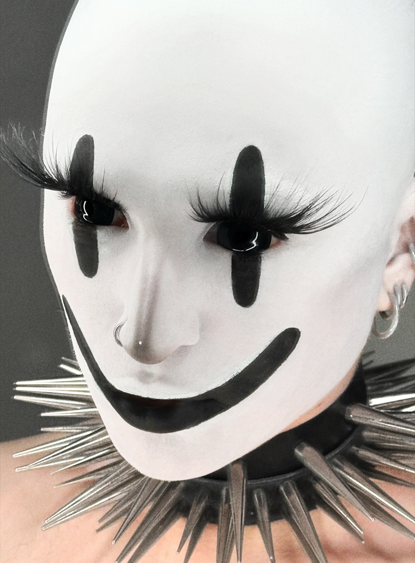 Bo Quinn in white face makeup with black graphic eyes, an exaggerated black smile and a metal spike collar