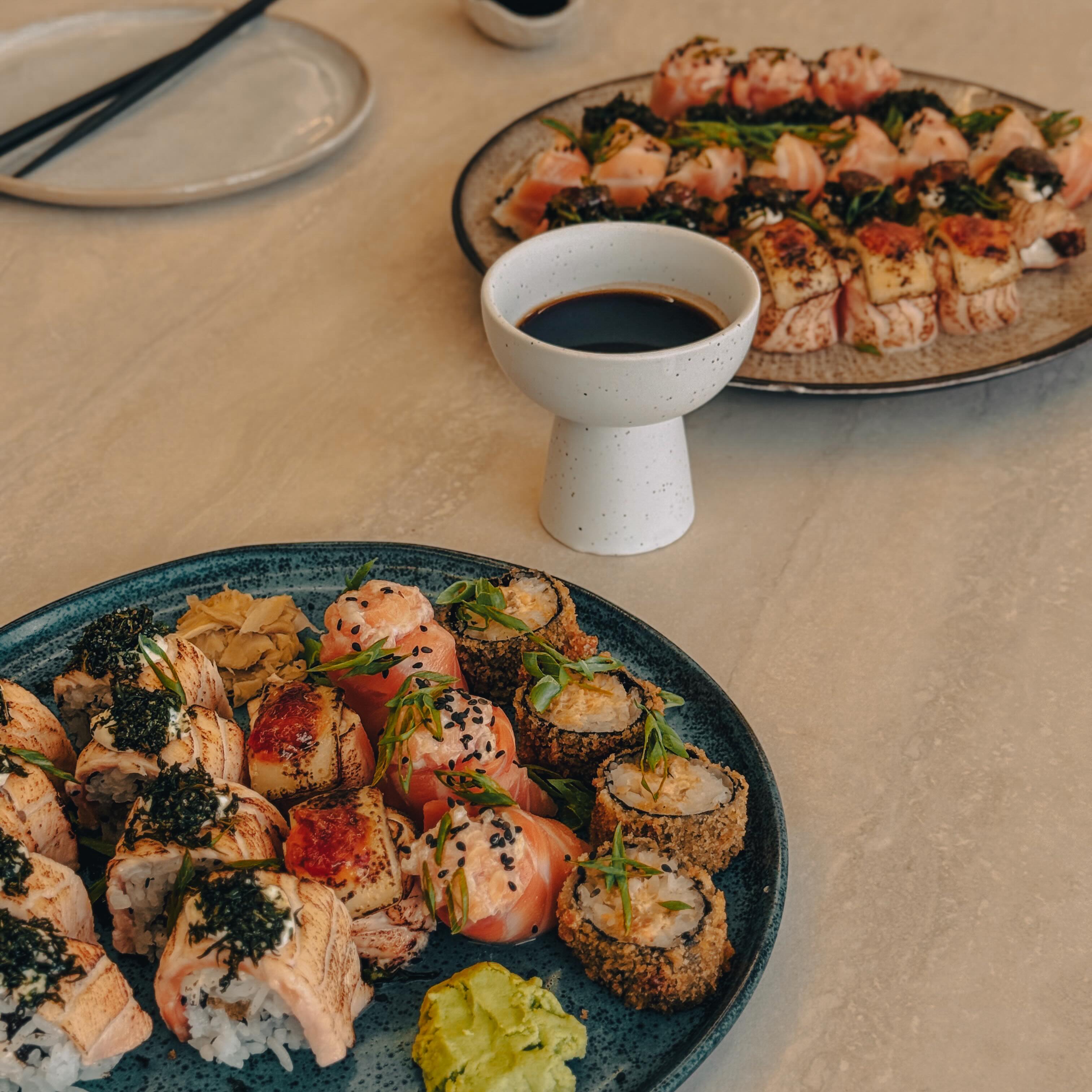 Duas travessas de sushi e sashimi servidas com molho shoyu