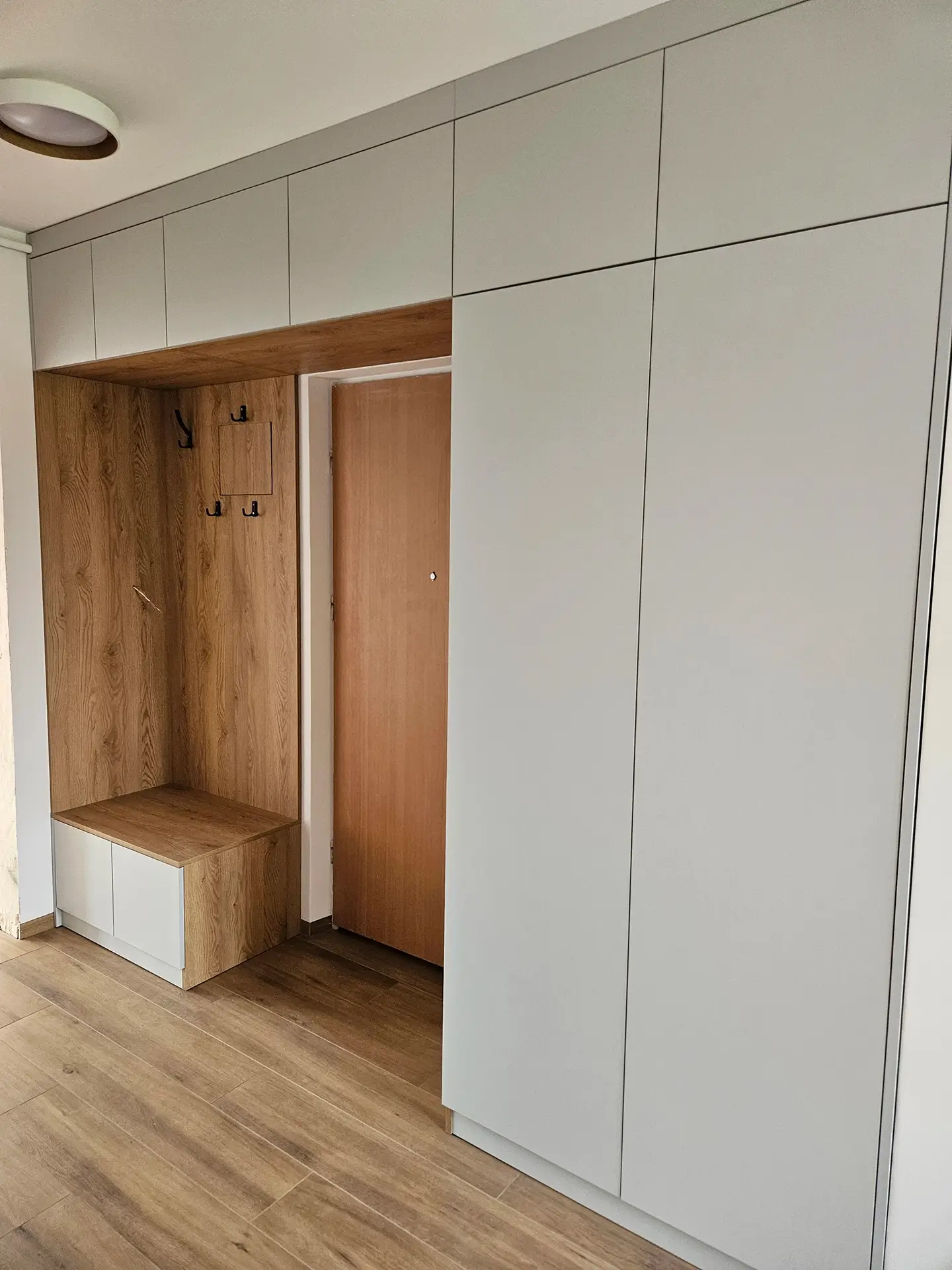 Pojemna zabudowa w sypialni z jasnymi frontami i centralną niszą z drewnianymi półkami.