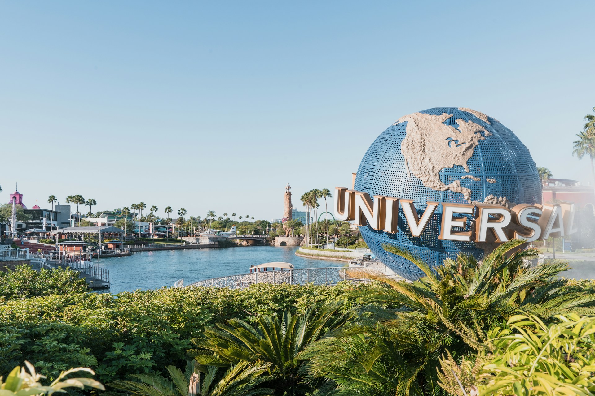 The Universal Studios globe sign beside a waterway surrounded by palm trees.