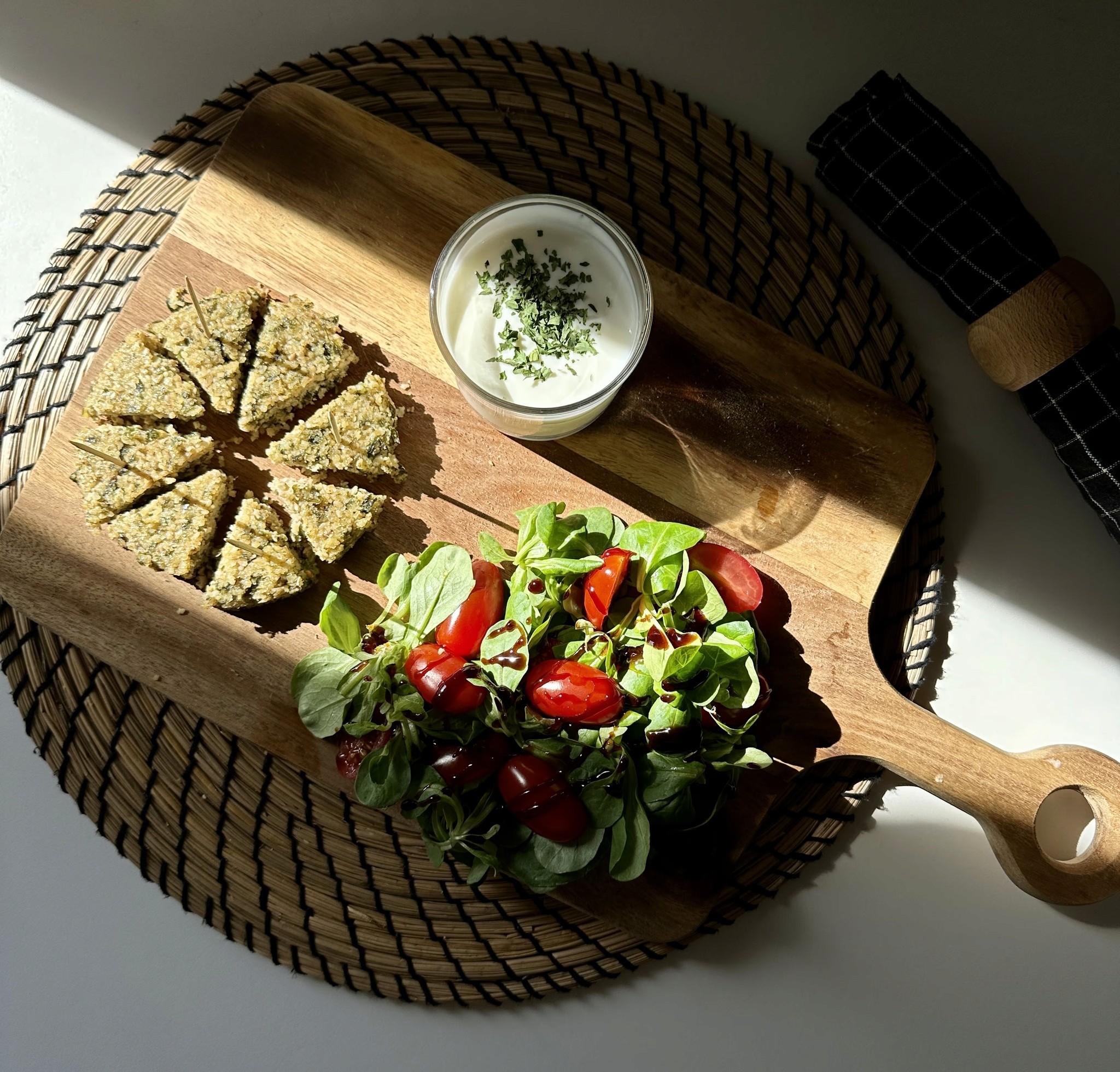 Galette végétale aux algues posée sur une planche en bois avec des tomates, de la salade et un yaourt