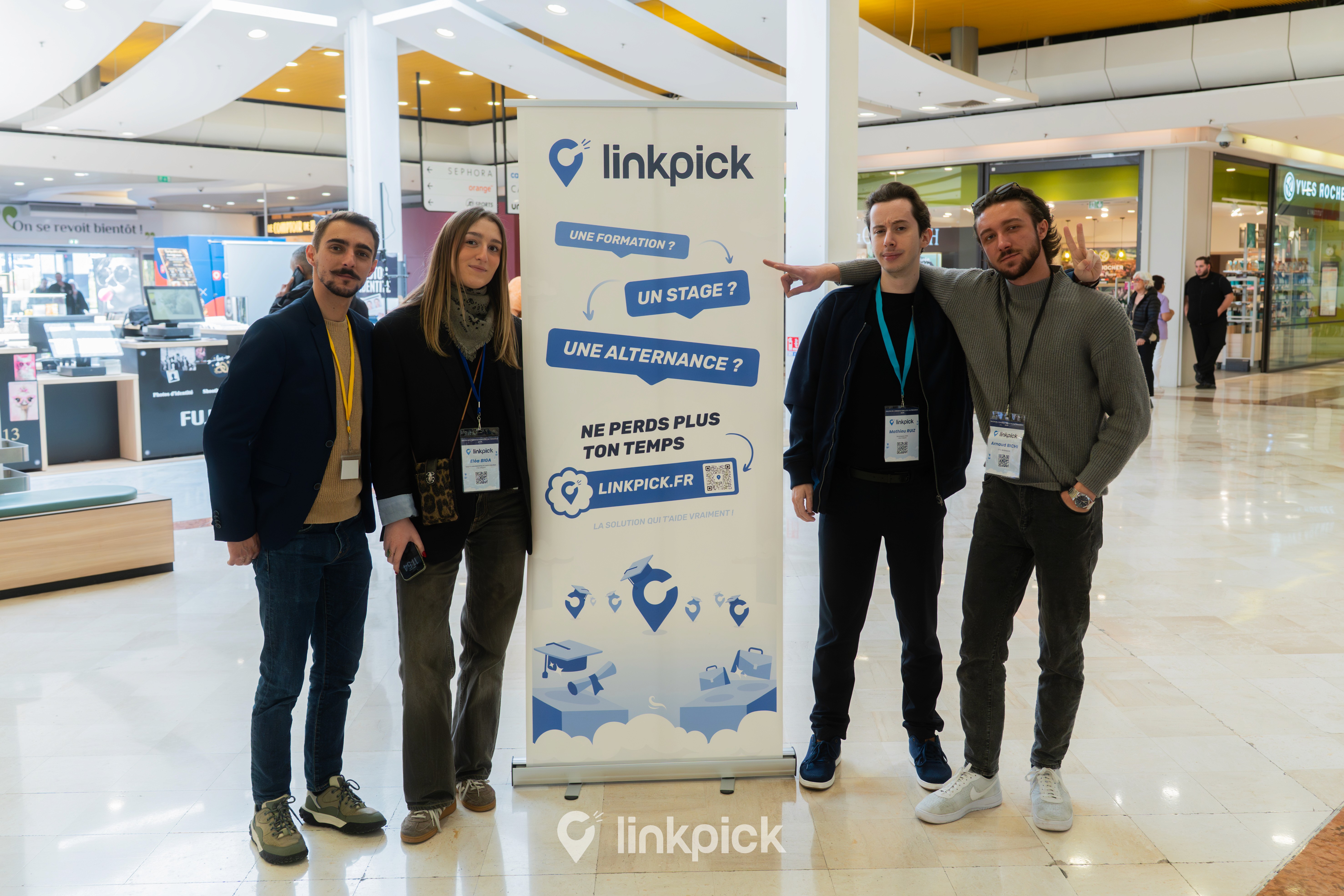 L'équipe Linkpick au complet pose avec le sourire derrière son oriflamme lors du Salon de l’Orientation et de l’Alternance. Le roll-up présente la solution Linkpick.fr pour trouver une formation, un stage ou une alternance. L'événement se déroule dans les allées lumineuses du centre commercial Grand Vitrolles.