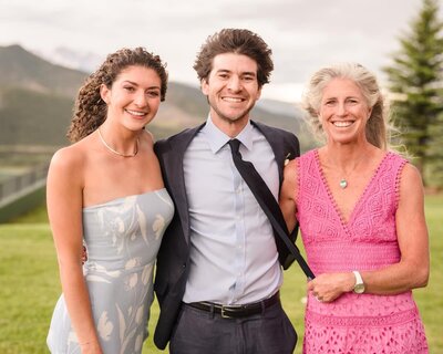 Three smiling guests standing together on a lawn at a mountain celebration