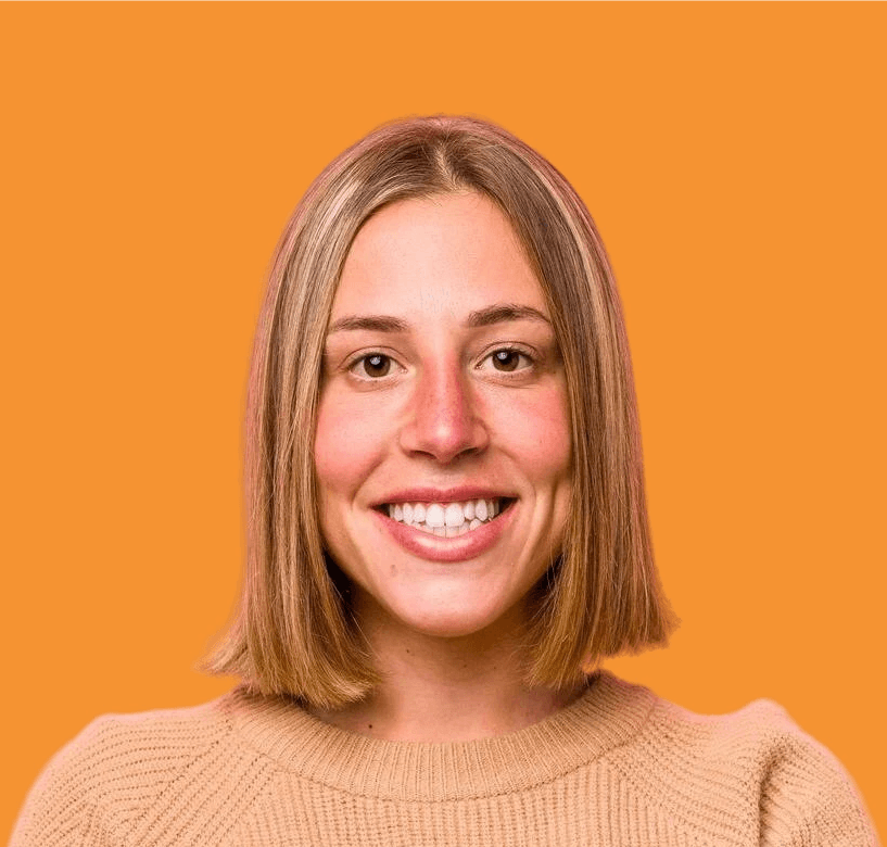 A young person with curly brown hair and a blue shirt stands against a plain light blue background, looking directly at the camera, exuding a calm and confident demeanor.