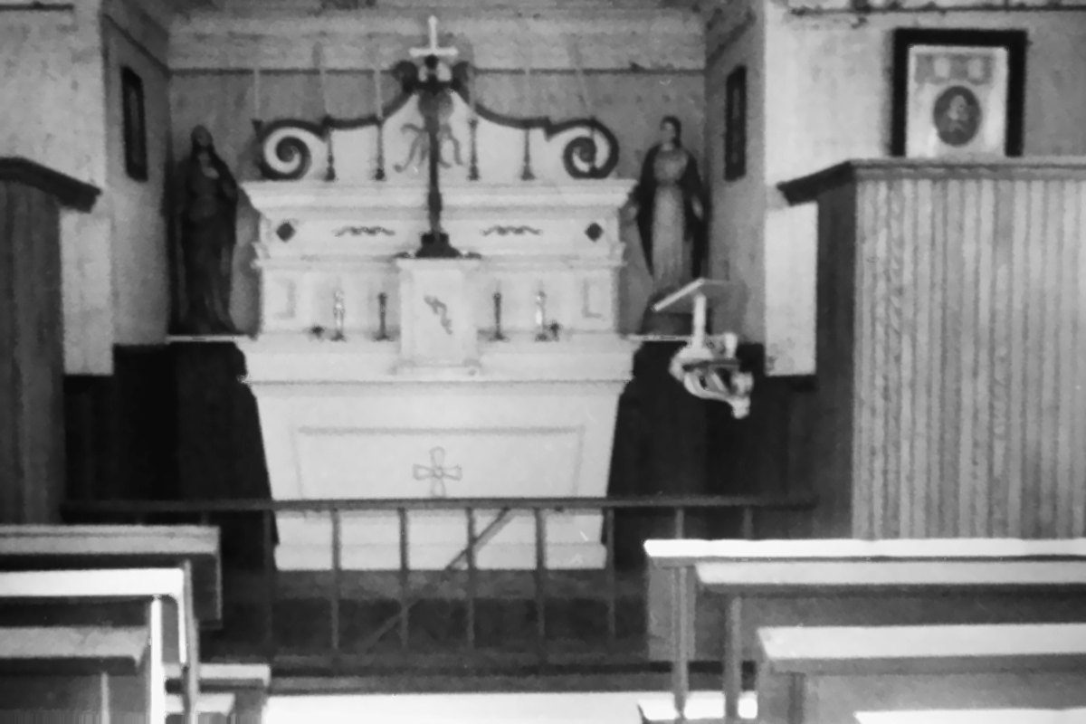Restored black-and-white photograph of the interior of St. Henry's Church: a white altar with statues, board-panelled walls, a rail and wooden benches