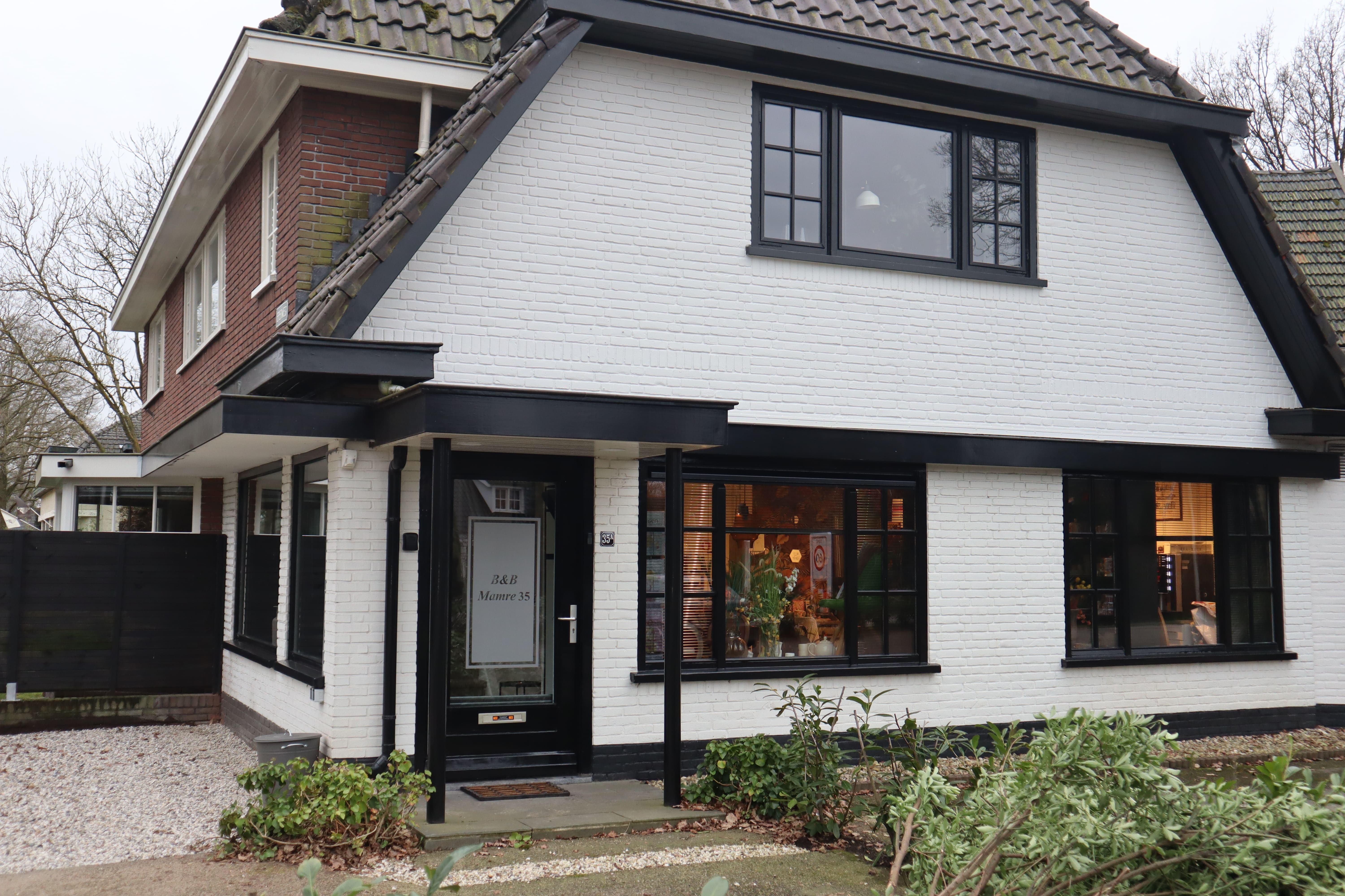 Wit huis met zwart kozijnen, een overdekte entree en een tuin voor het huis.