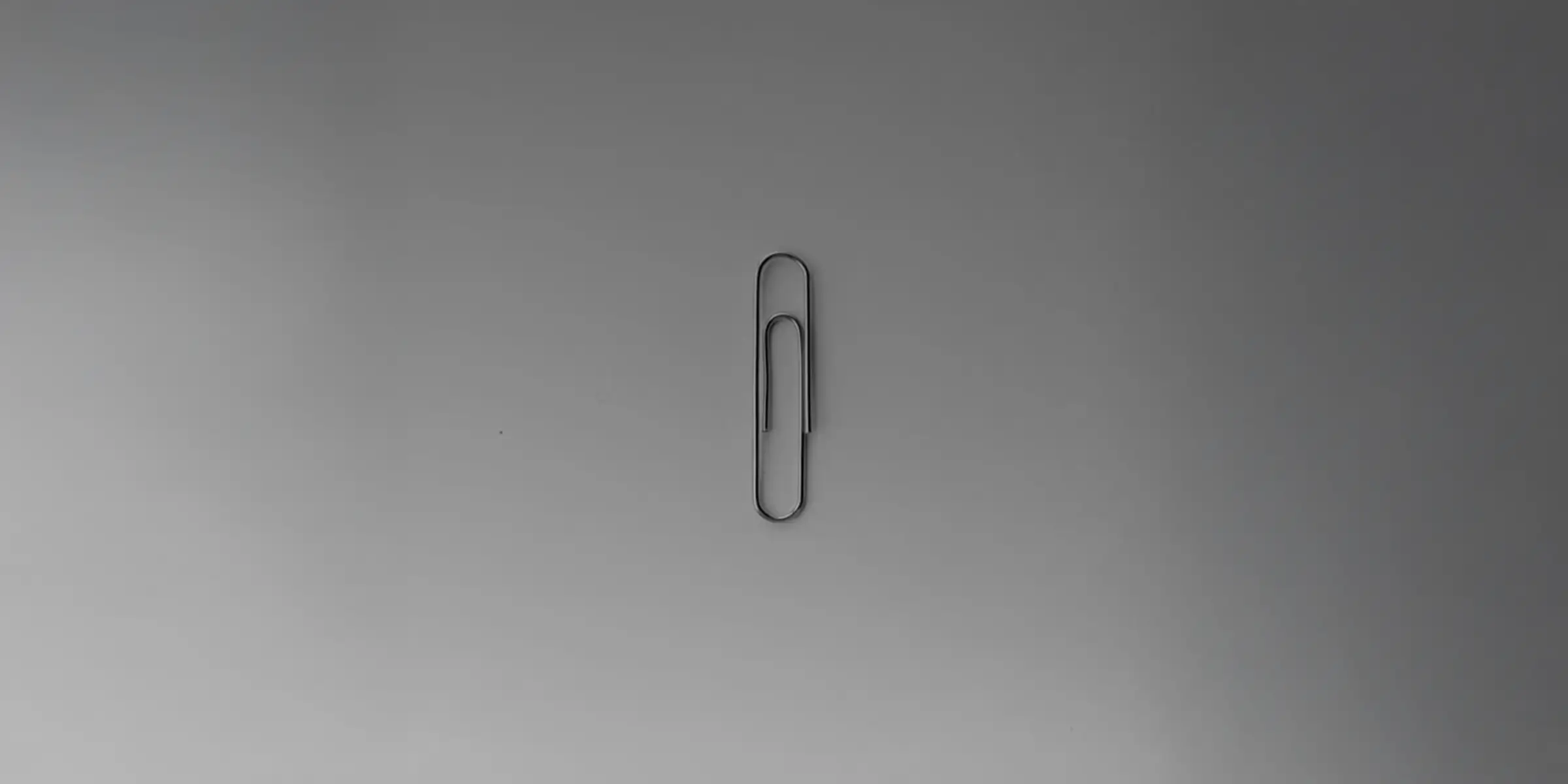 Minimal black-and-white image of a single paperclip centred on a neutral background, representing simplicity, focus, and restraint.