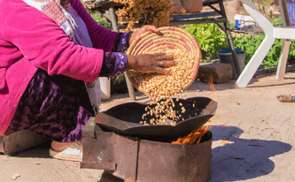 Woman pours corn into a pan over a fire